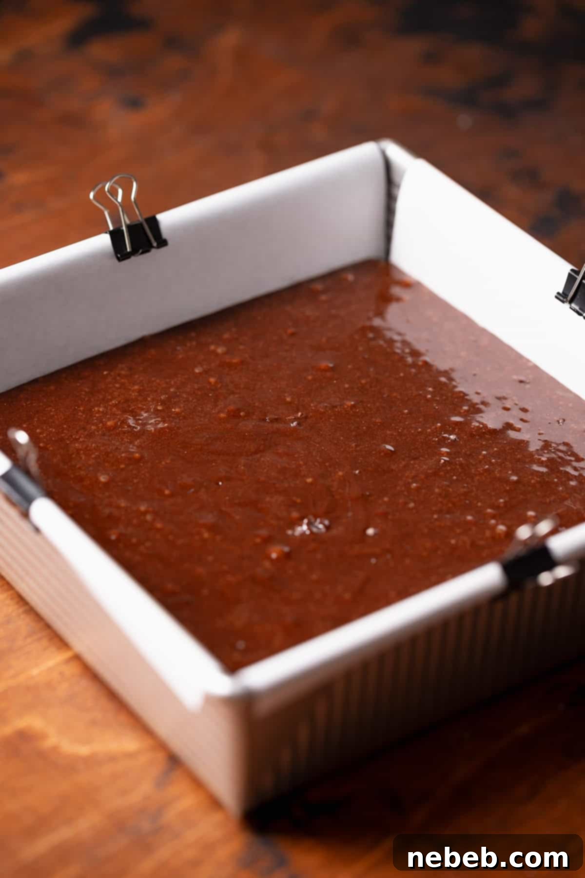 A square metal baking pan filled with unbaked brownie batter, ready for the oven.