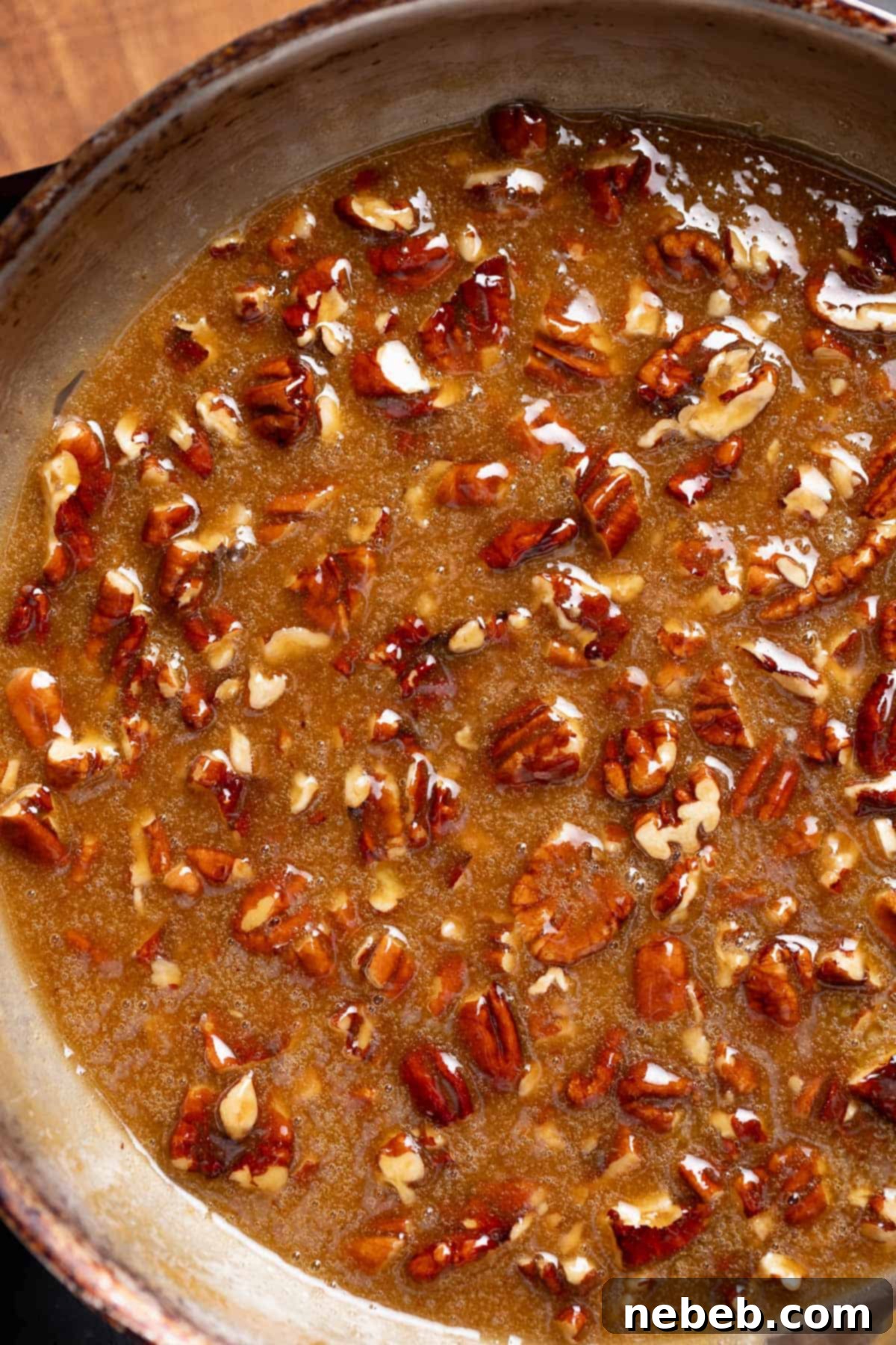 The pecan pie filling in a pan after the pecans and butter have been added and stirred, looking glossy and rich.