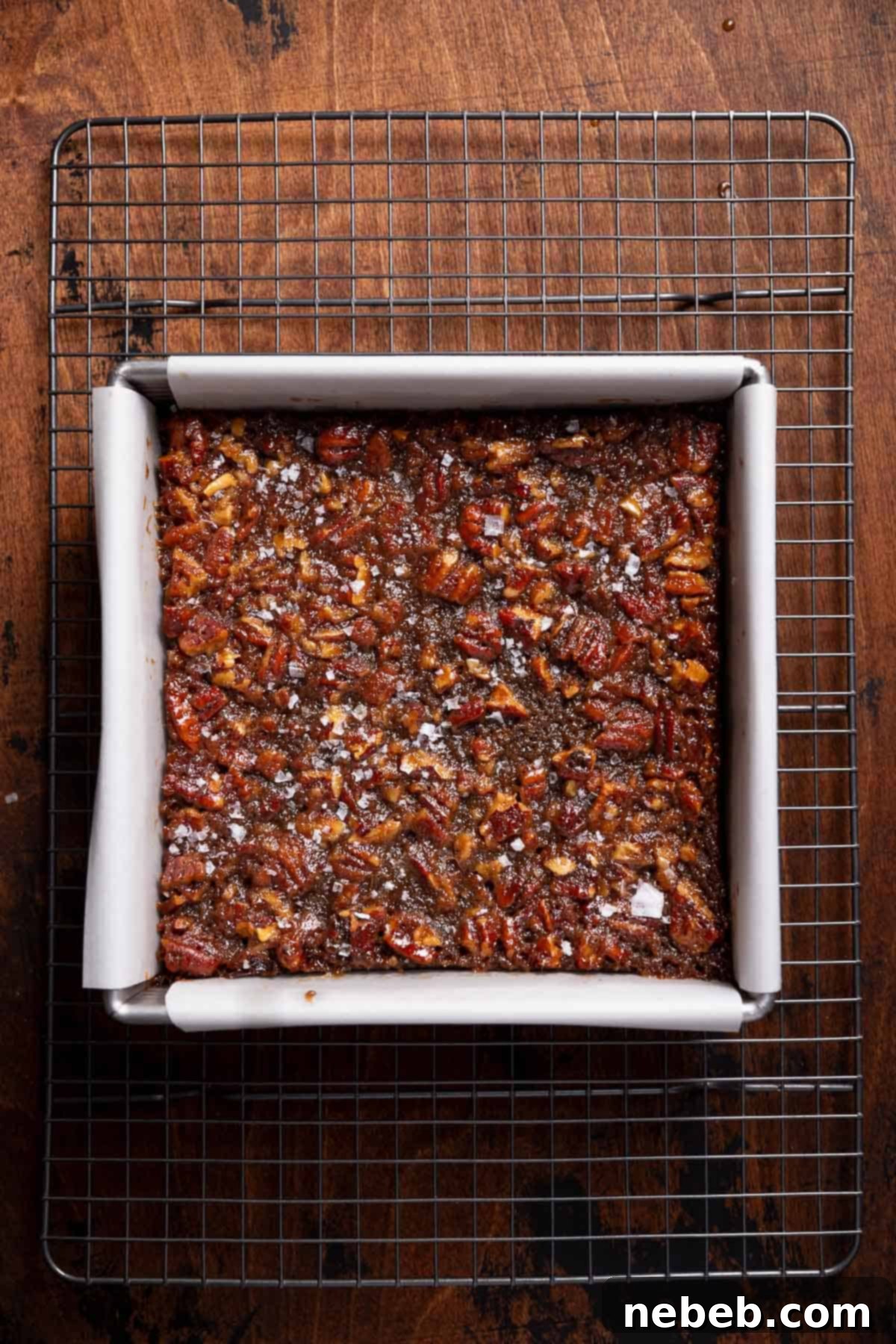 A pan of freshly baked pecan pie brownies cooling on a wire rack, sprinkled with flaky sea salt.