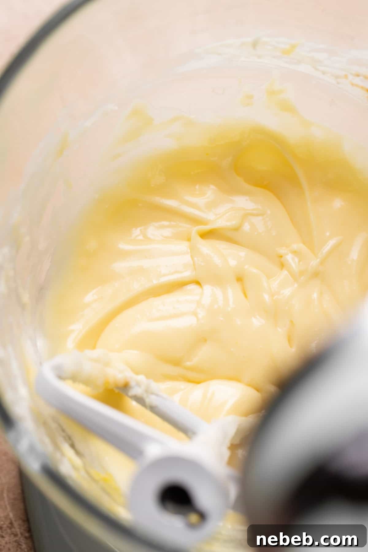 A glass mixing bowl with creamed butter, cream cheese, granulated sugar, and eggs, ready to be mixed.