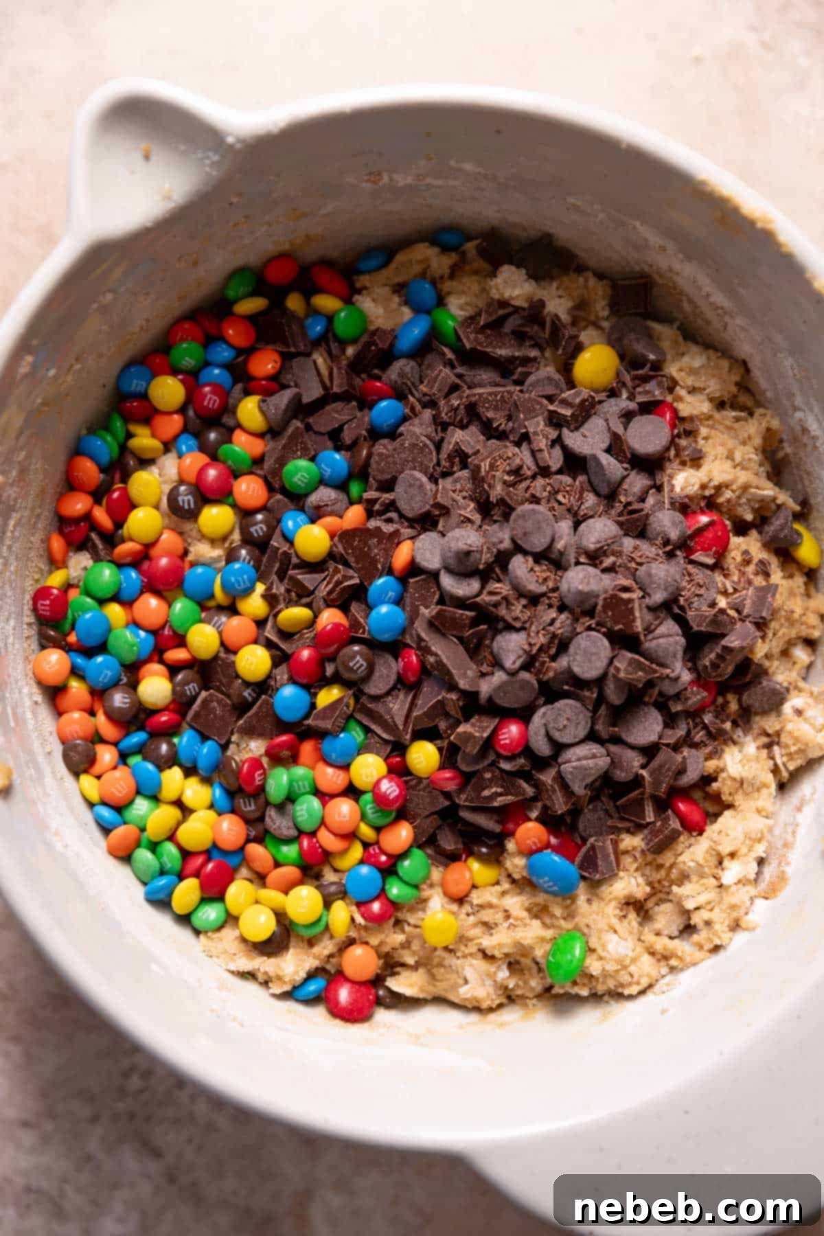 Ultimate Monster Cookie Bars 6 A mixing bowl with the oatmeal cookie dough with mm and chocolate chips on top.