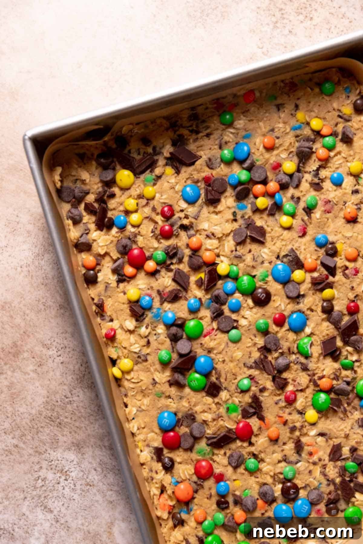 Ultimate Monster Cookie Bars 7 A baking pan with the peanut butter cookie dough pressed into the pan with extra candies and chocolate chips on top.