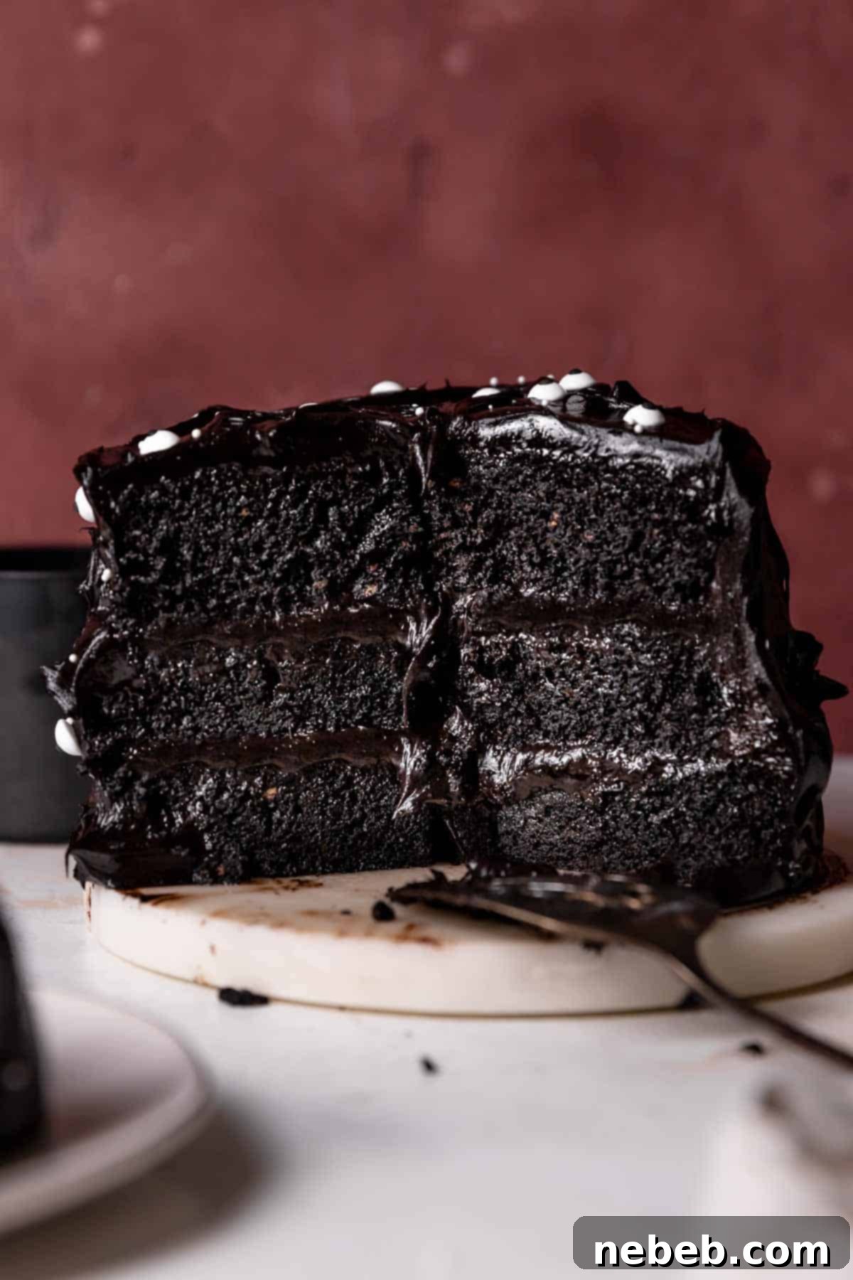 Black velvet cake cut in half on a white marble platter, showcasing its dark interior and creamy frosting.