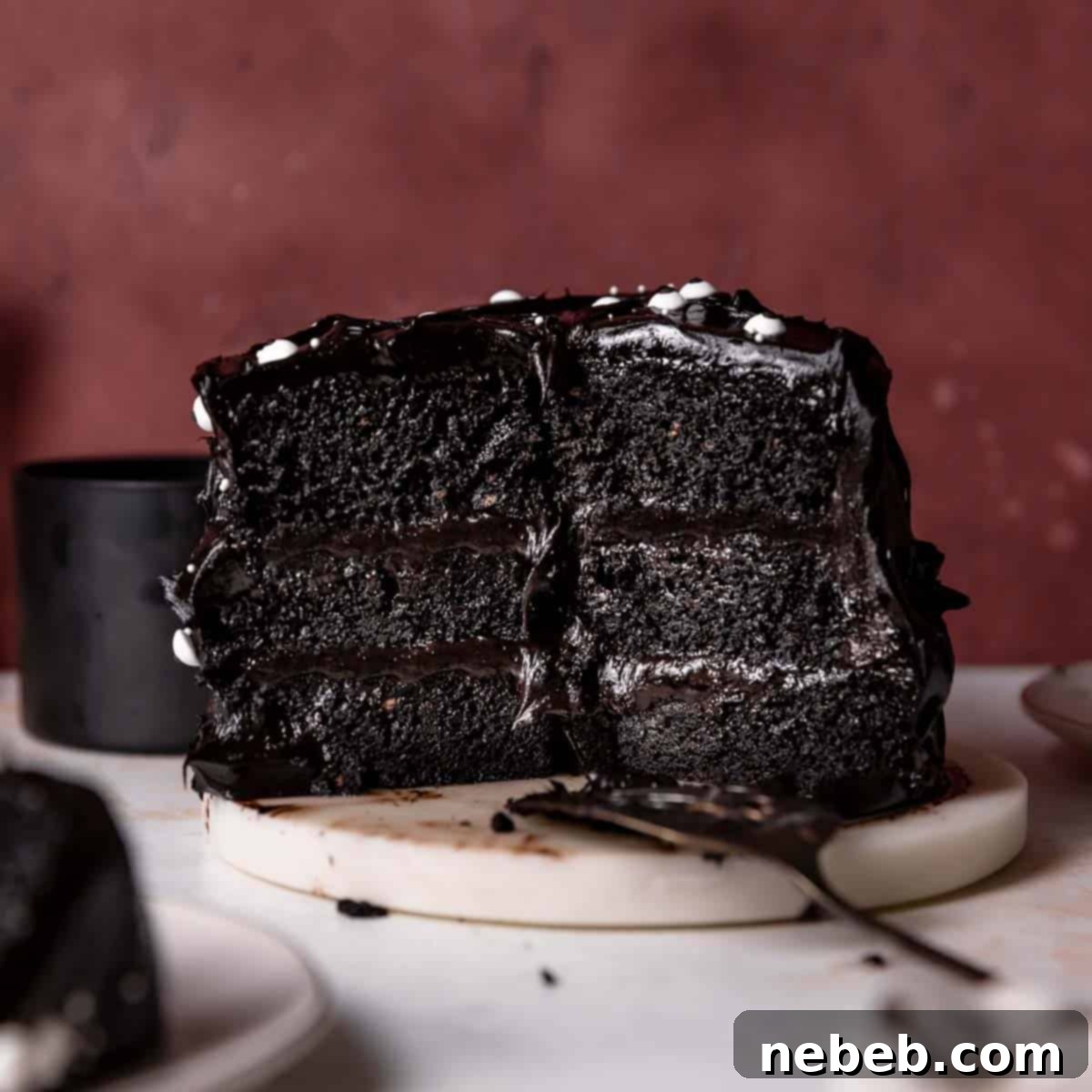 Black velvet cake cut in half on a white marble platter, showcasing its dark interior and creamy frosting.