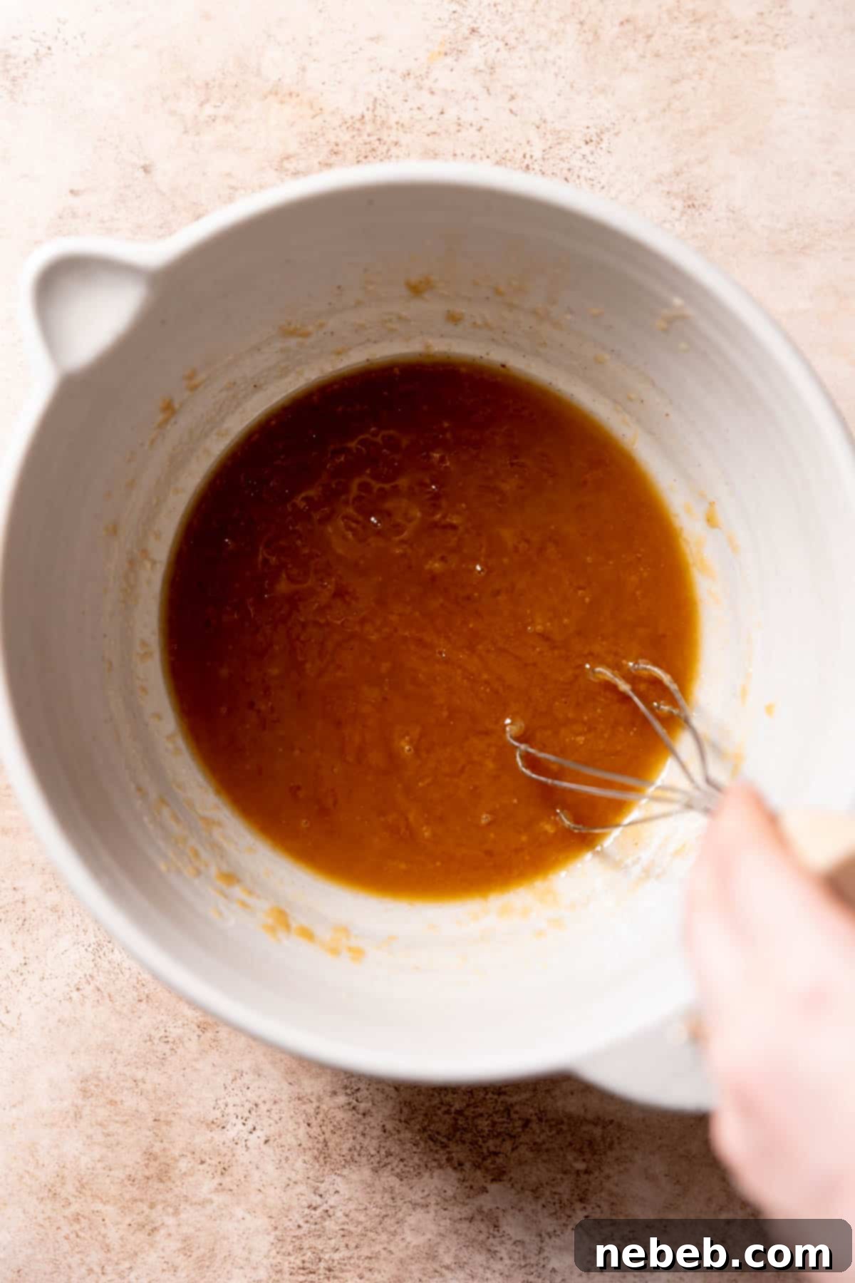 Melted butter and both granulated and brown sugars being vigorously whisked together in a large mixing bowl.