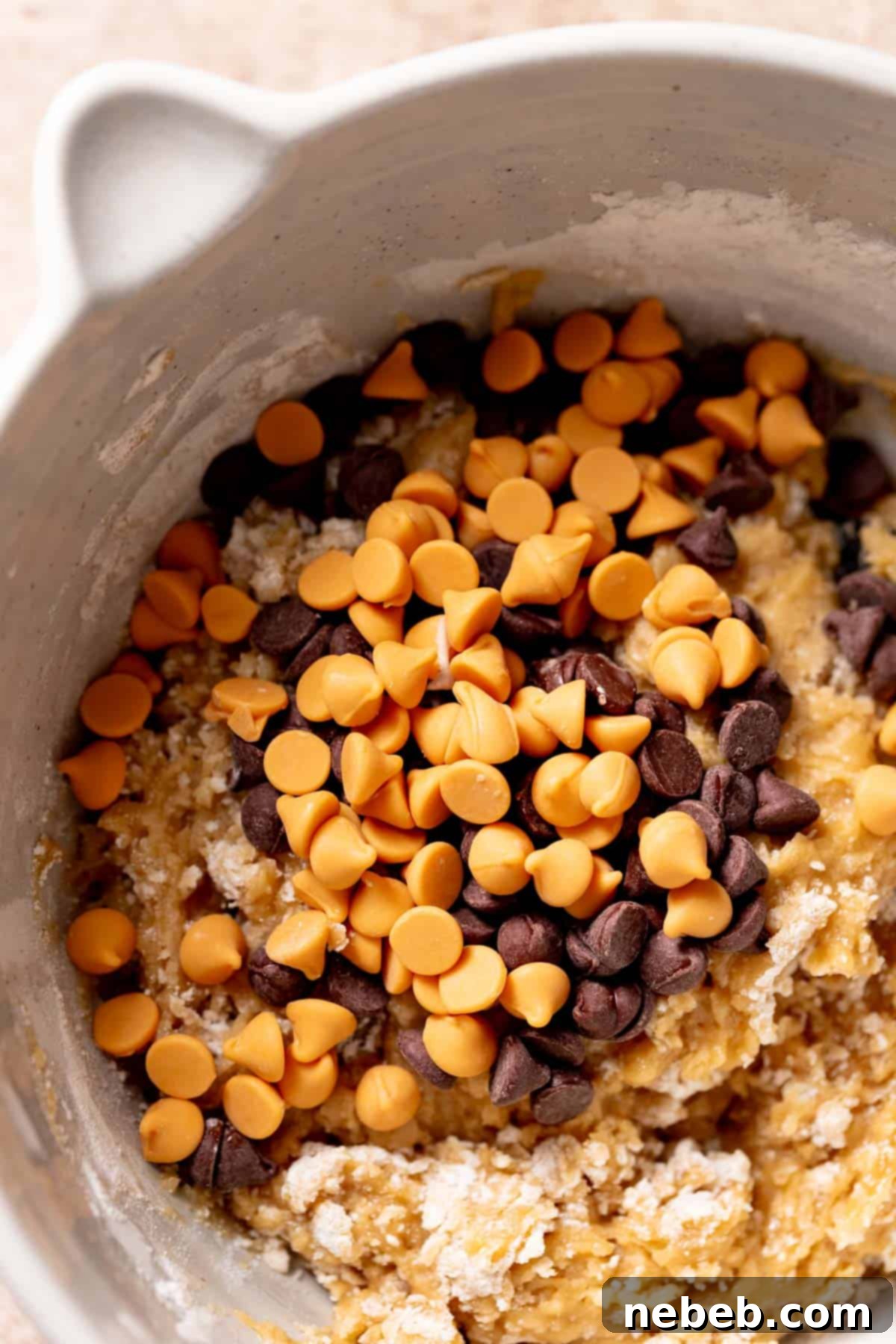 An enticing view of butterscotch and chocolate chips generously sprinkled on top of the cookie dough in a mixing bowl, ready to be incorporated.