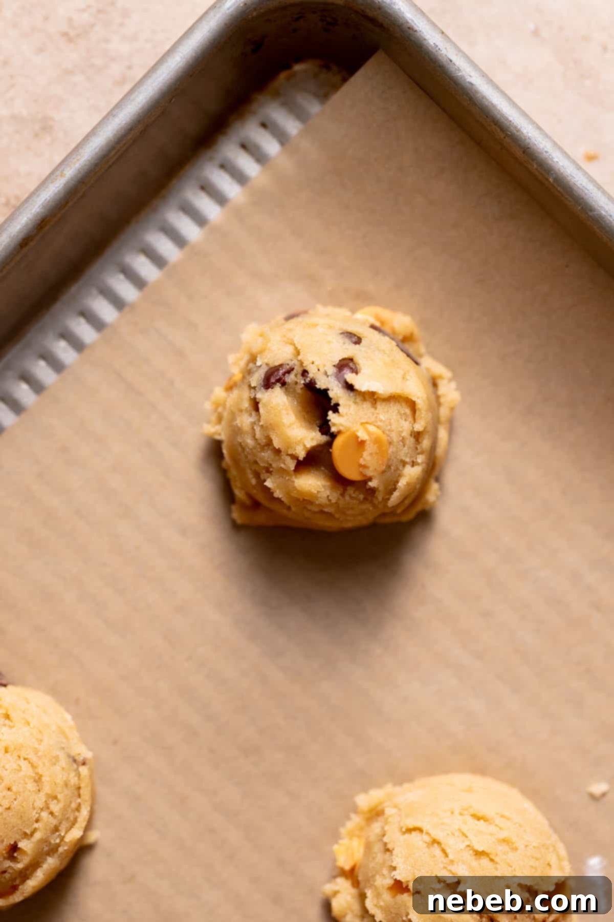 A perfectly portioned ball of butterscotch chocolate chip cookie dough resting on a parchment-lined baking sheet, ready for the oven.