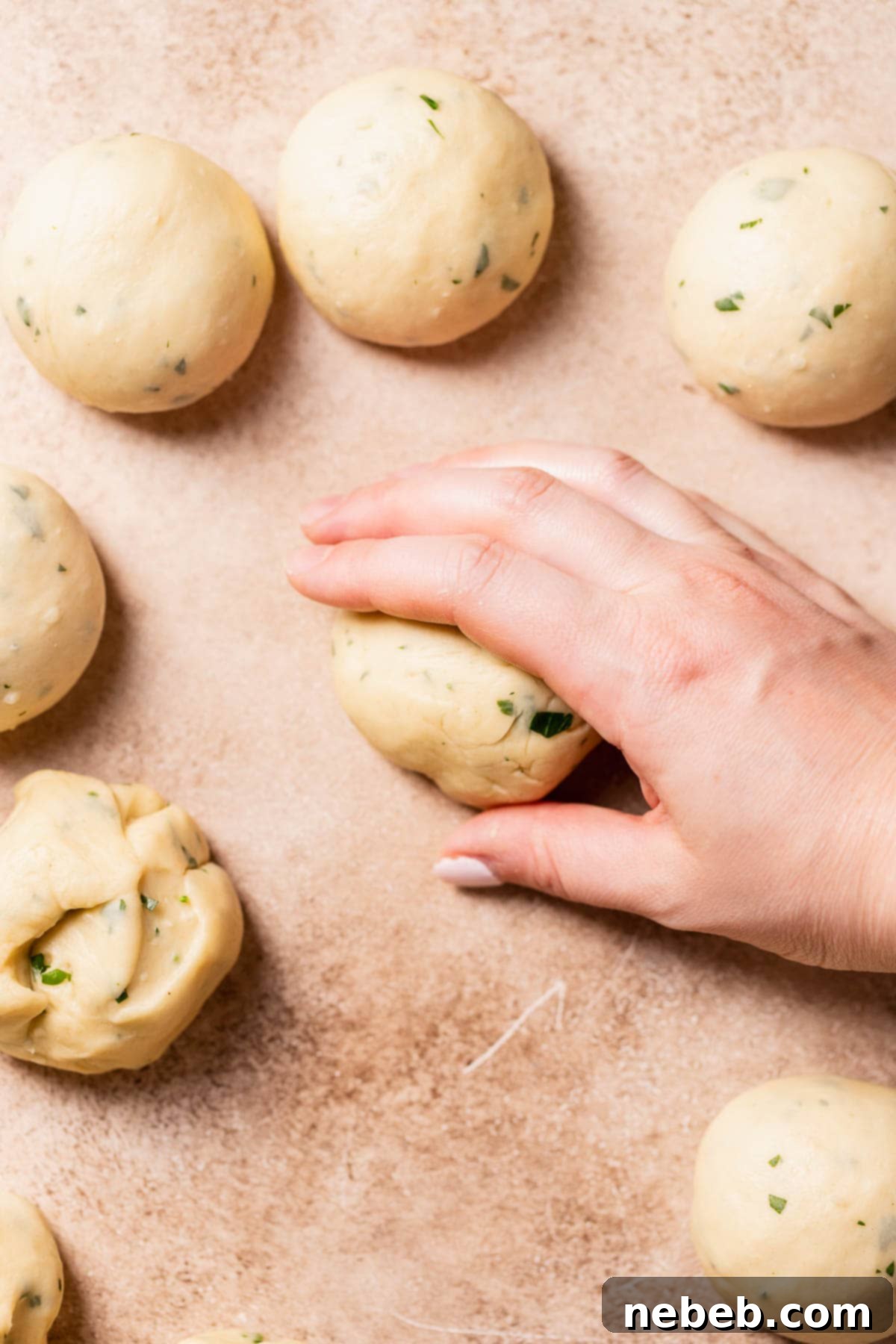 A hand rolling the garlic dough into dough balls.