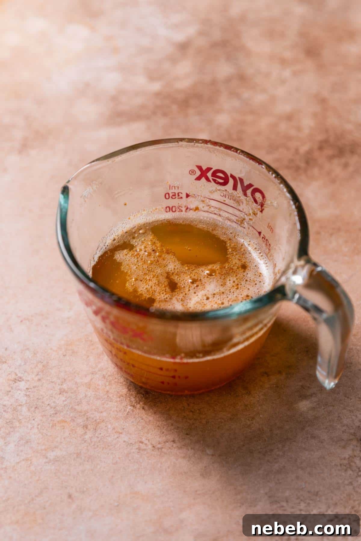 A clear glass measuring cup holding rich, amber-colored melted brown butter, ready for the next step in the recipe.