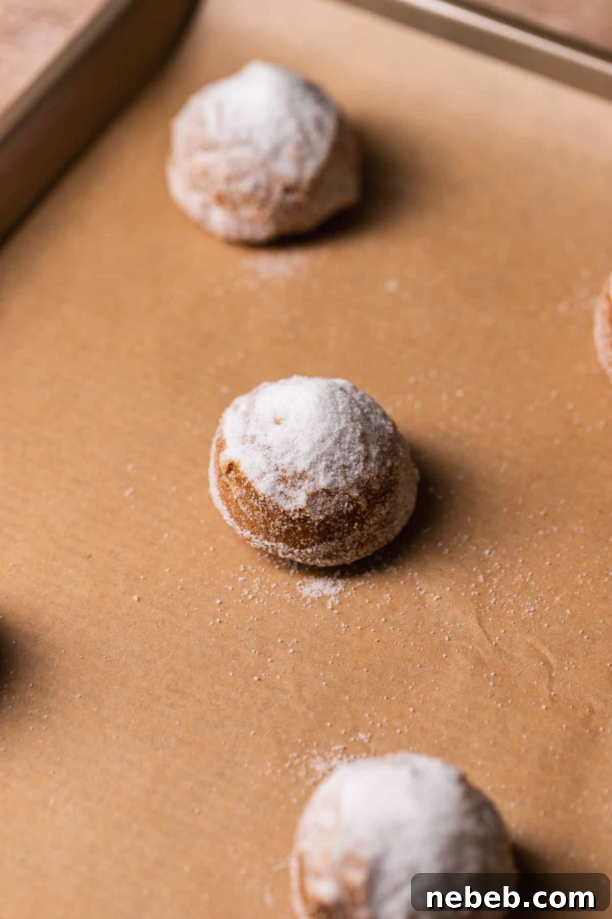 A single molasses cookie dough ball on a baking sheet, generously coated with white granulated sugar, with an extra pile on top, illustrating the technique for perfect crinkles.