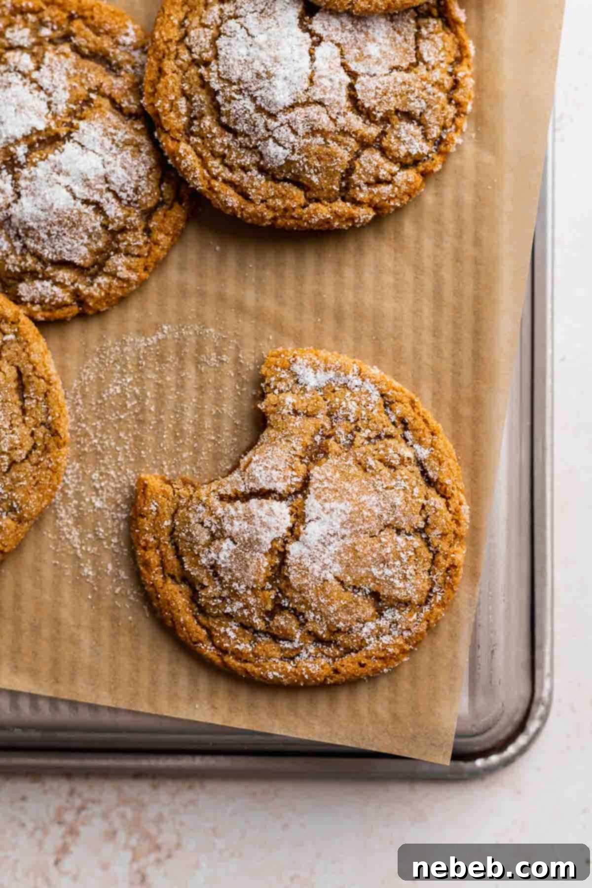 A single brown butter molasses crinkle cookie with a bite taken out, resting on parchment paper on a baking tray, revealing its soft, chewy interior.