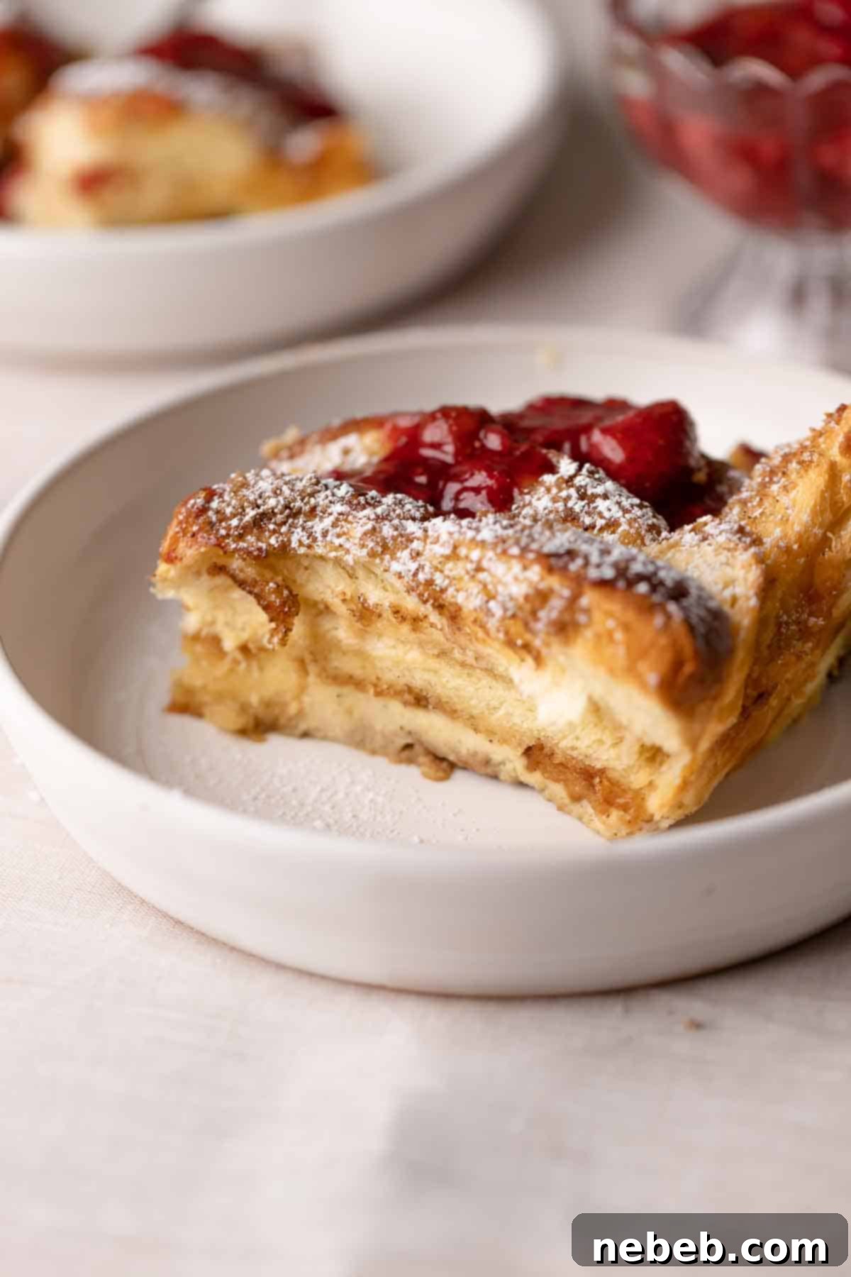 A perfectly golden slice of brioche french toast casserole, lightly dusted with powdered sugar and adorned with fresh strawberries, ready to be served.