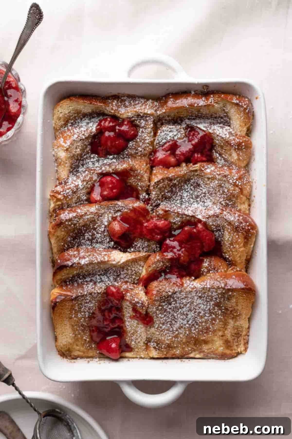 A full brioche french toast casserole dish, generously dusted with powdered sugar and garnished with fresh strawberries, ready to be served.