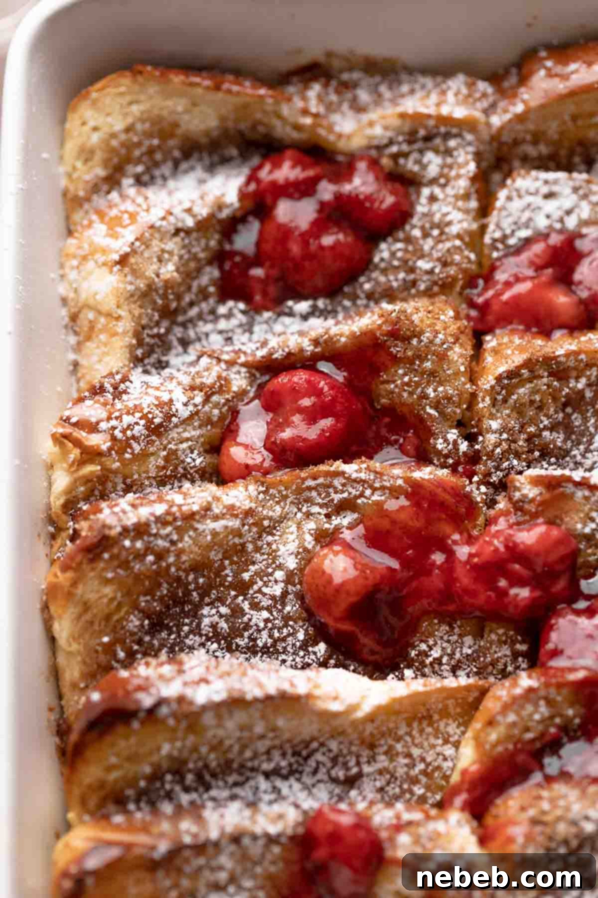 A close-up of a serving of brioche french toast casserole, garnished with powdered sugar and fresh strawberries, highlighting its texture.