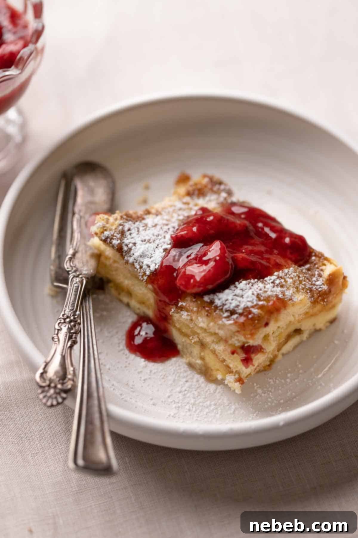 A single slice of baked brioche french toast casserole on a white plate, showcasing its golden crust and soft interior.