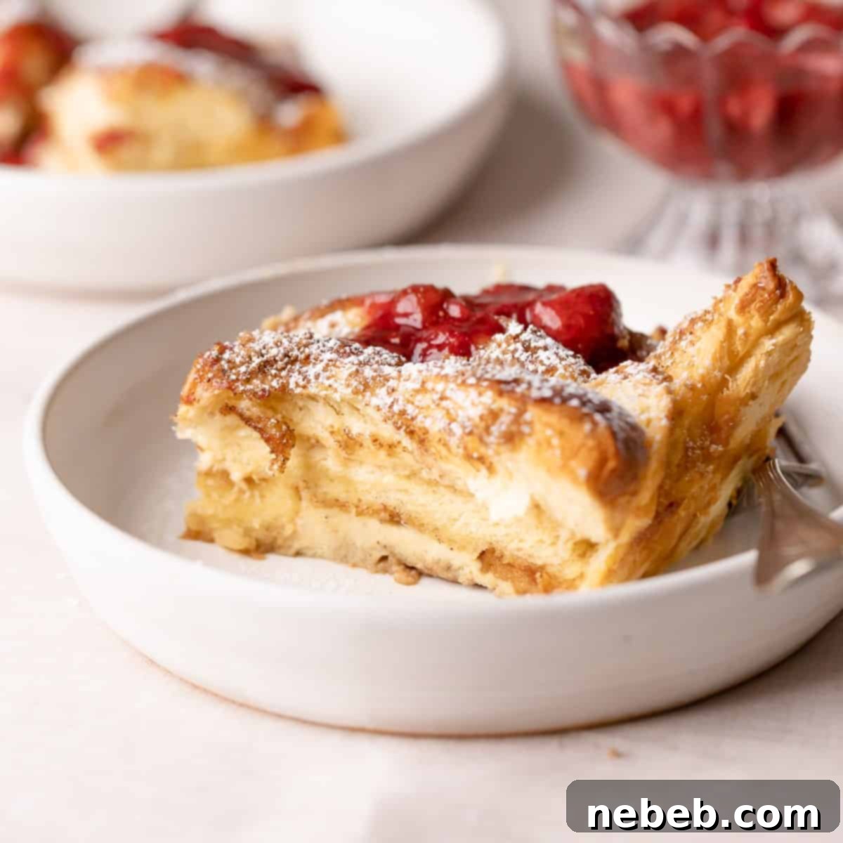 A delectable slice of brioche french toast casserole on a plate, beautifully dusted with powdered sugar and adorned with fresh berries.
