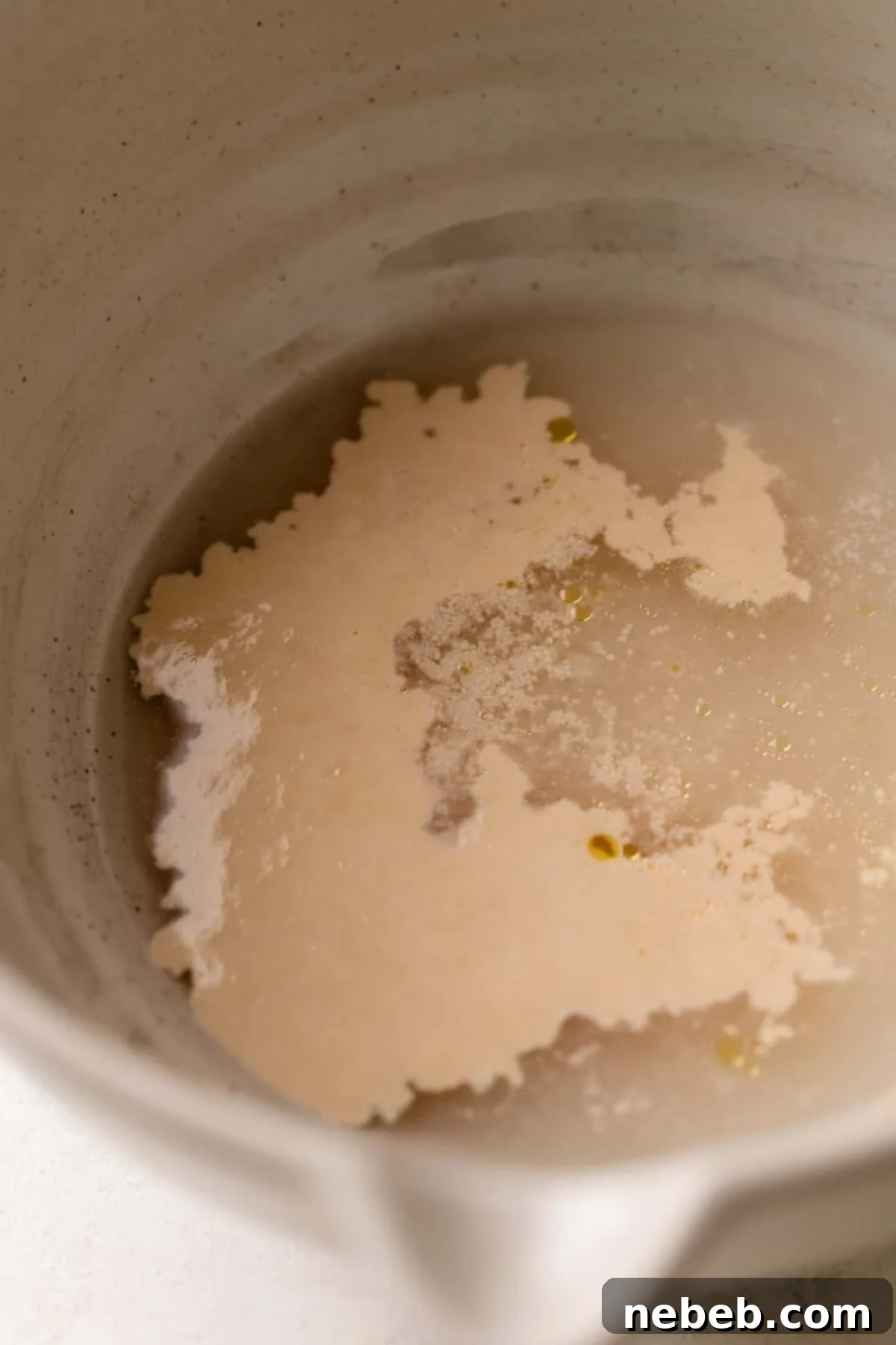 Perfectly Soft and Chewy Homemade Pizza Dough 3 Yeast showing foaming activity when mixed with warm water and honey in a bowl.