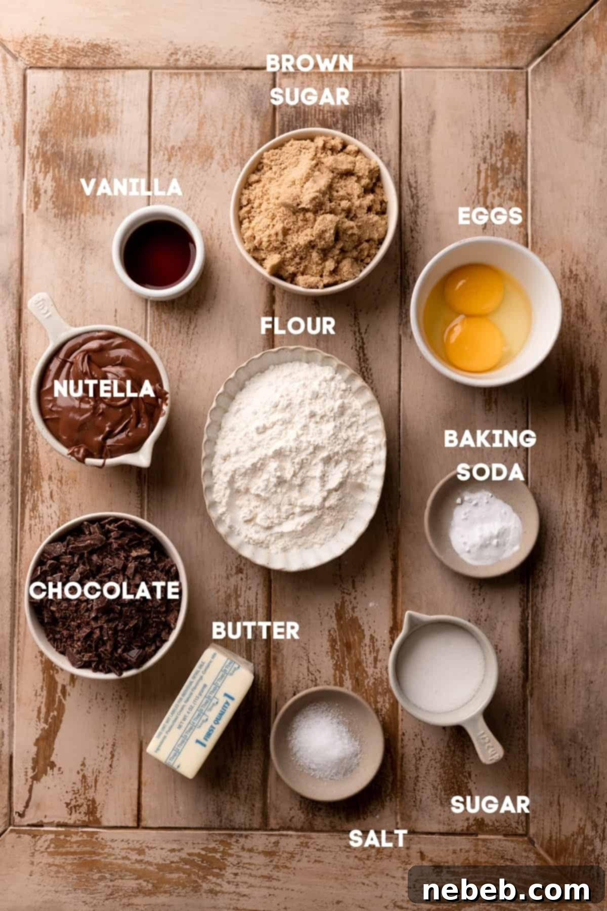 Various ingredients for chocolate filled cookies, including Nutella, chocolate chips, butter, and sugars, neatly arranged in bowls with labels.