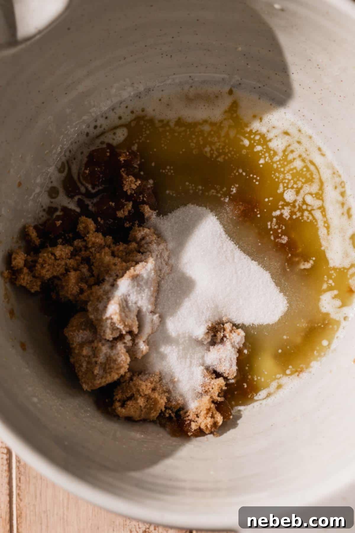 A mixing bowl containing melted butter, granulated sugar, and light brown sugar, perfectly combined and ready for the next wet ingredients.