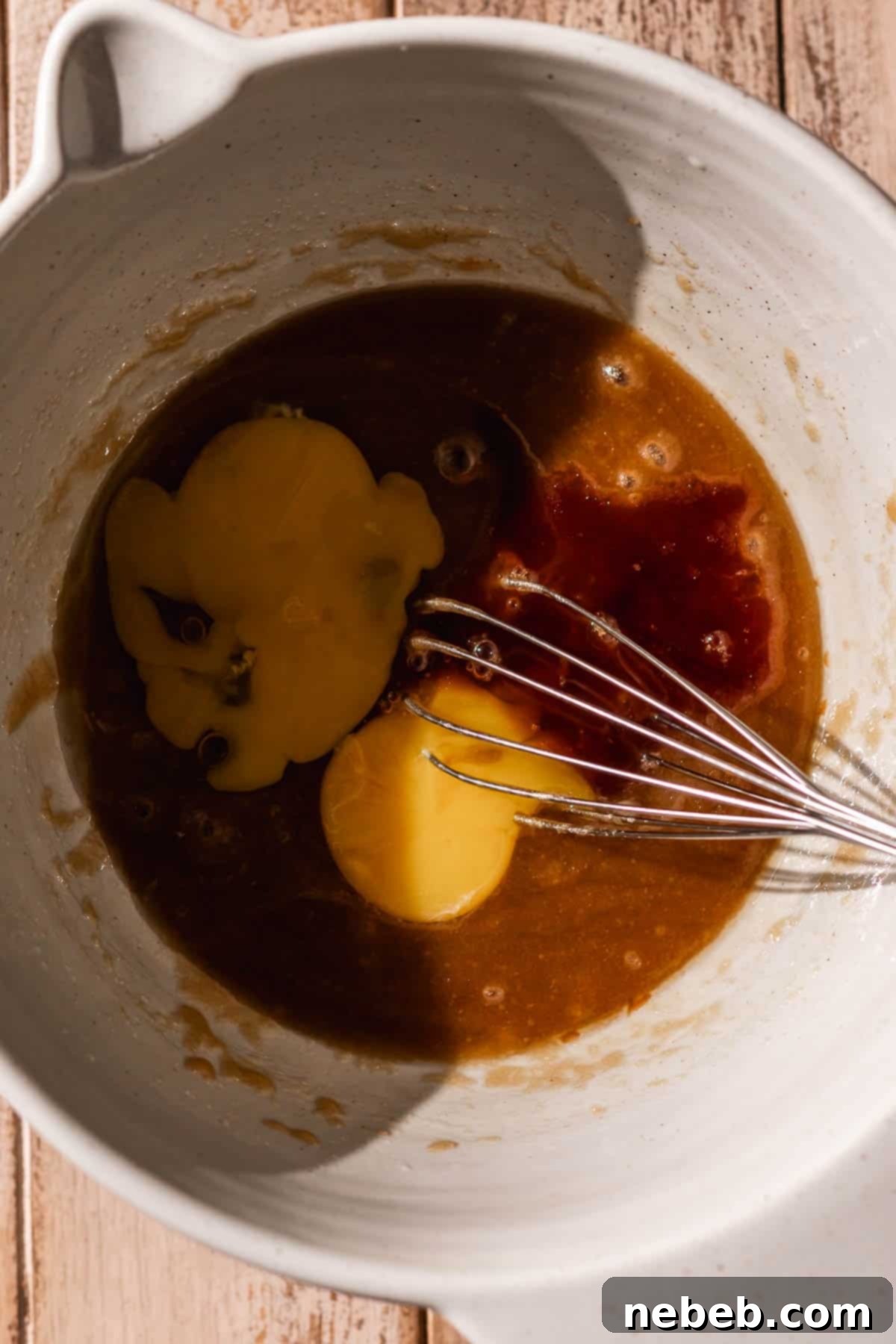 Room temperature egg and vanilla extract being whisked into the butter and sugar mixture in a large bowl, creating a smooth, emulsified wet base.