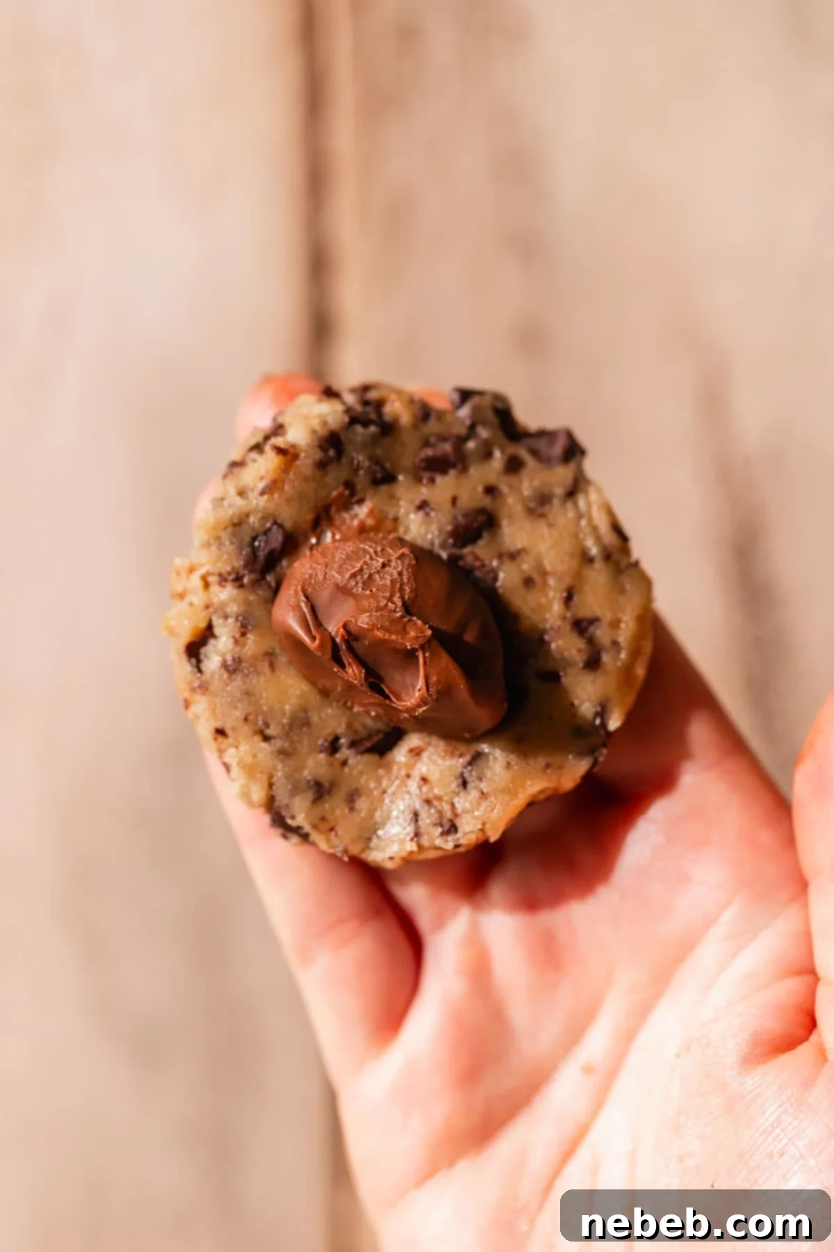 A hand expertly molding cookie dough around a frozen chocolate hazelnut filling, ensuring a complete seal for the chocolate filled cookies.
