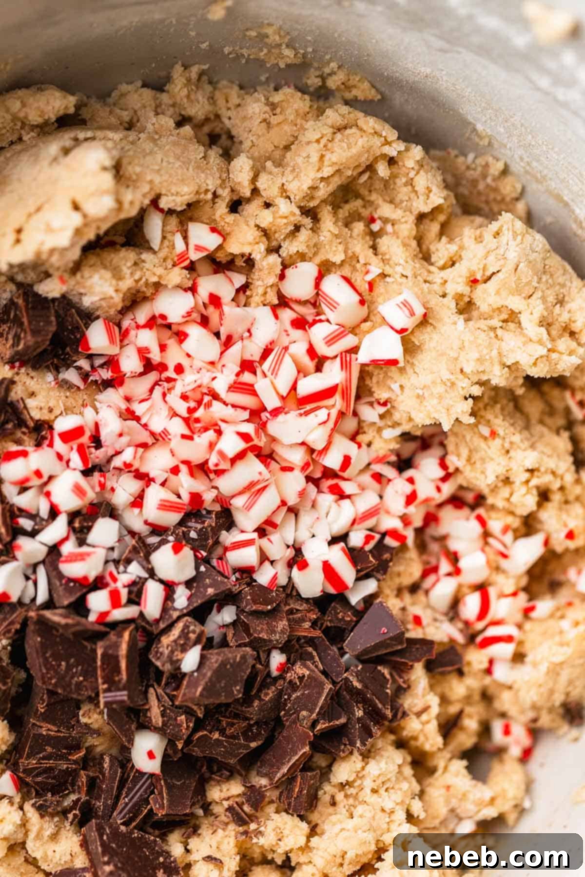 A mixing bowl with the dark chocolate and candy cane pieces being folded into the cookie dough with a spatula.