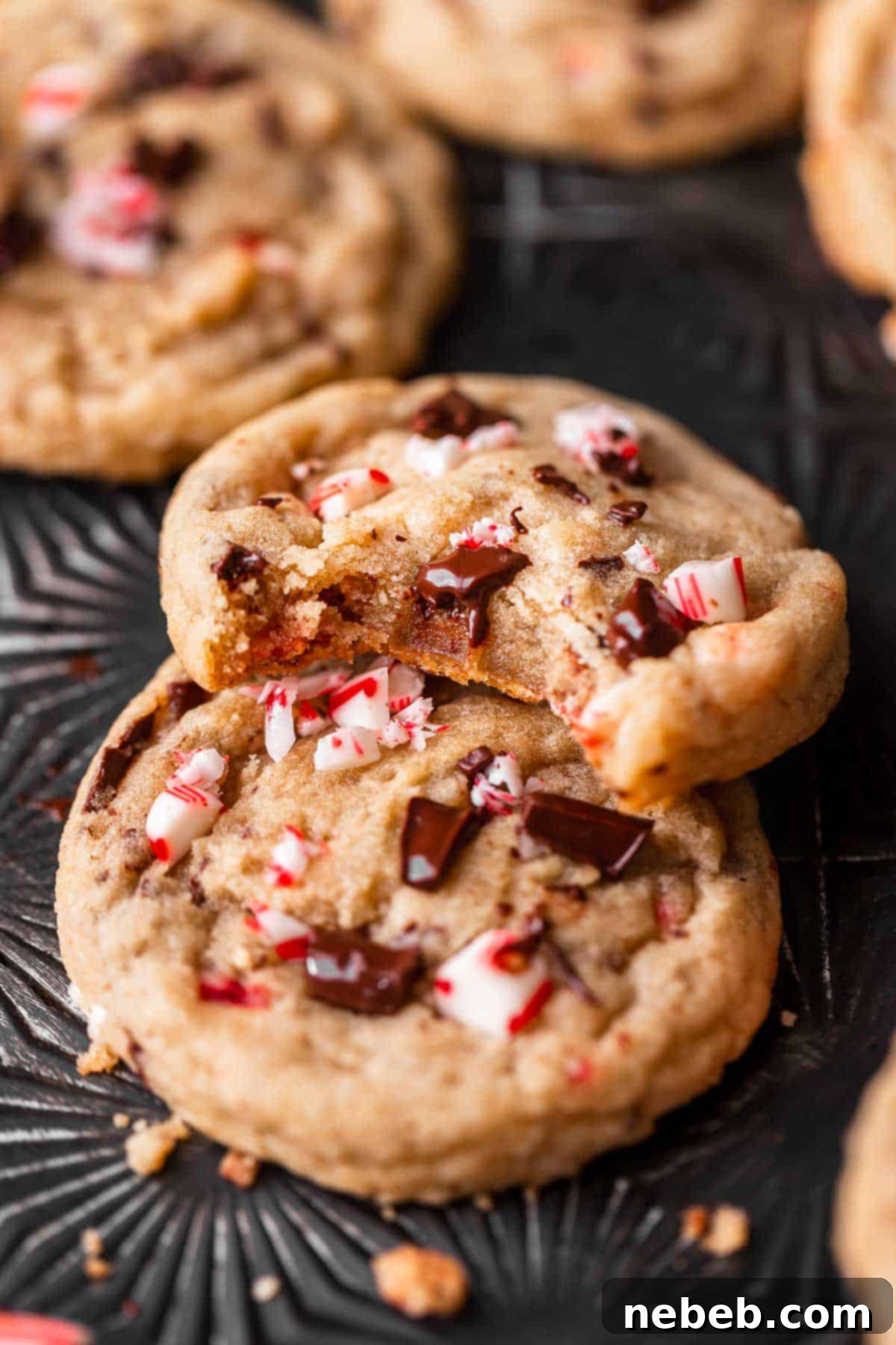 A peppermint chocolate chip cookie leaning on another cookie with a bite taken out of it, showing the soft, chewy interior with melted chocolate and peppermint pieces.