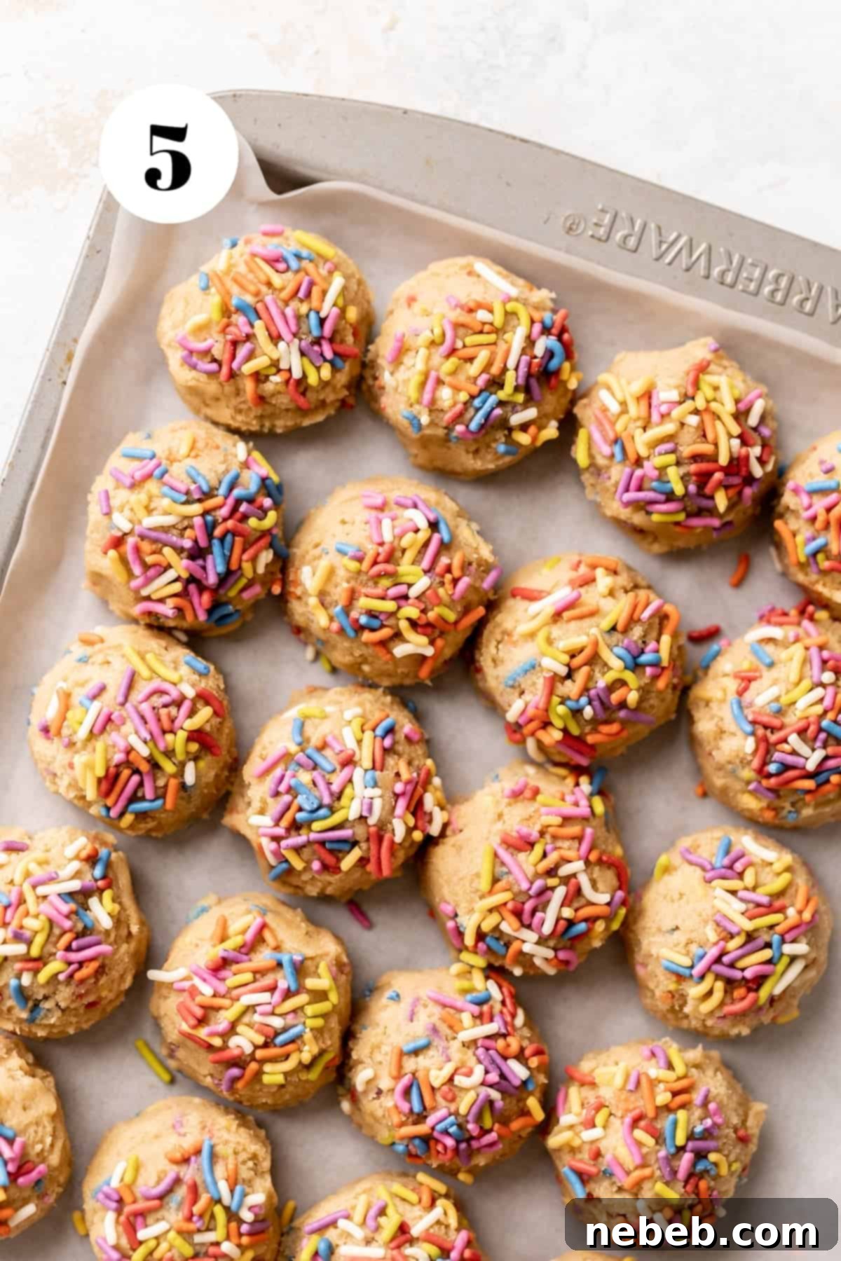 sugar cookie dough balls topped with rainbow sprinkles on a baking tray.