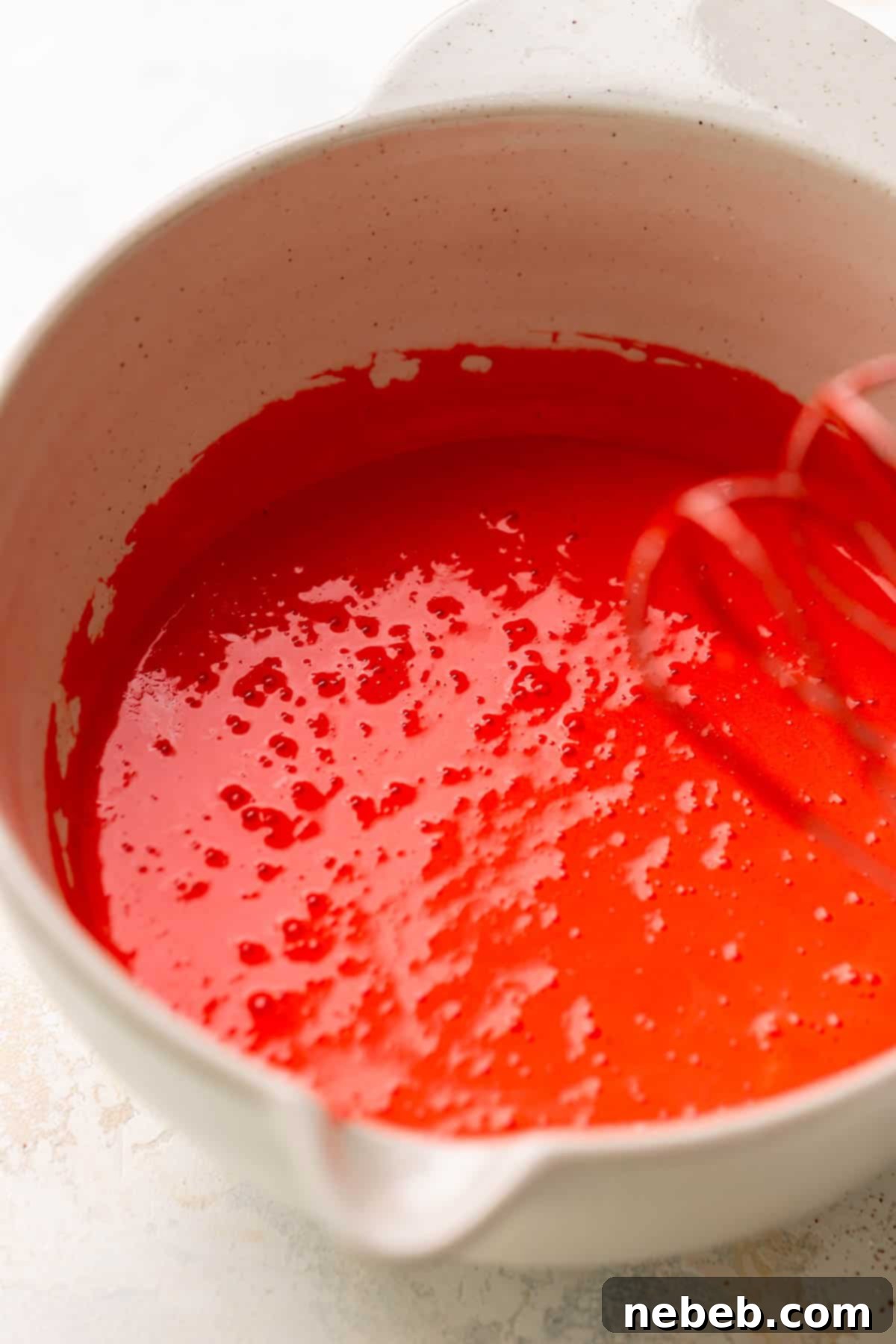A mixing bowl with the bright red brownie batter after mixing wet ingredients.