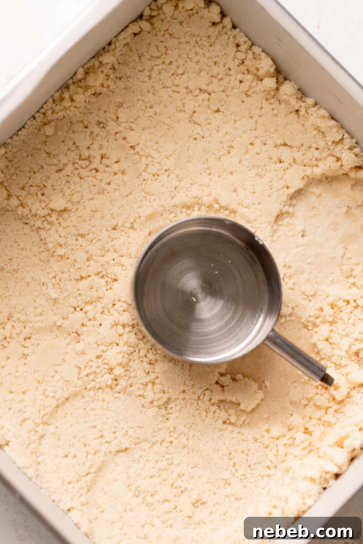 a measuring cup pressing the shortbread crust into the baking pan.