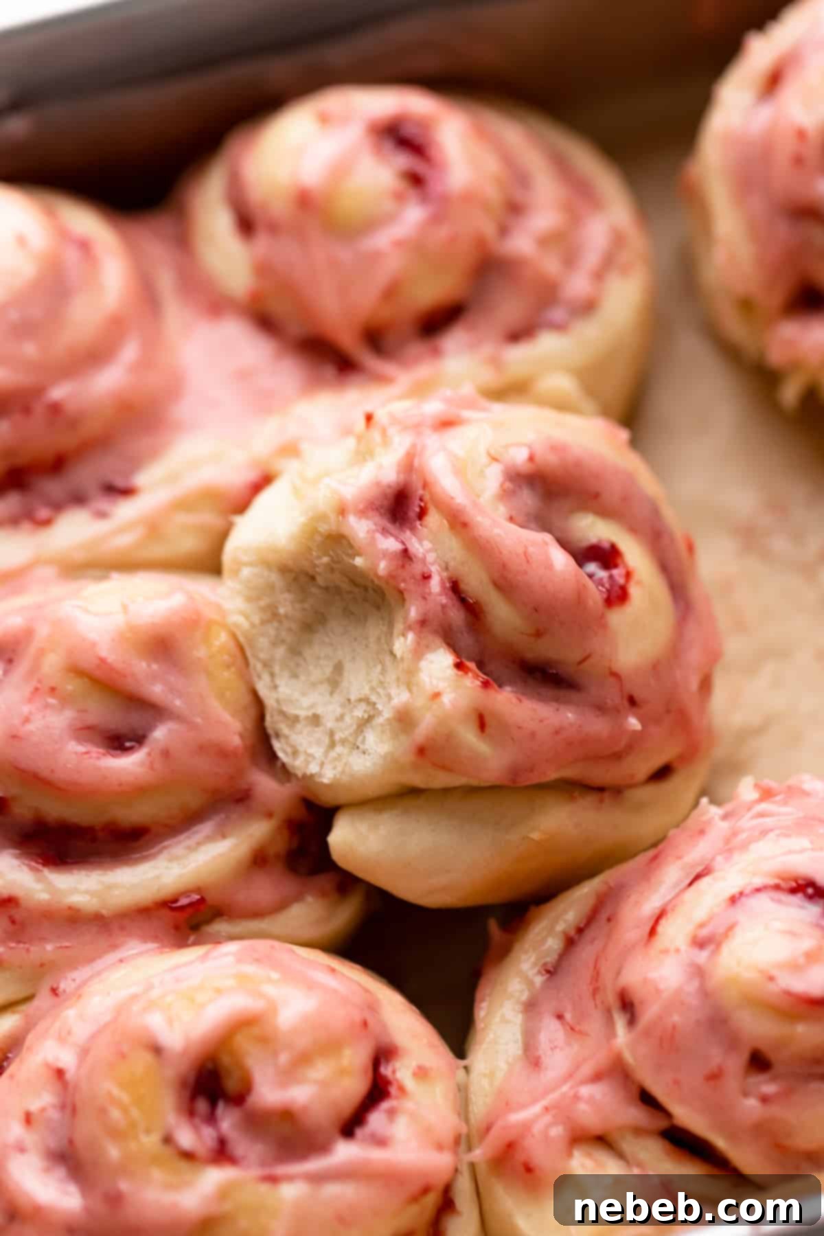 strawberry cinnamon rolls sitting in a baking pan, generously covered in strawberry cream cheese icing.