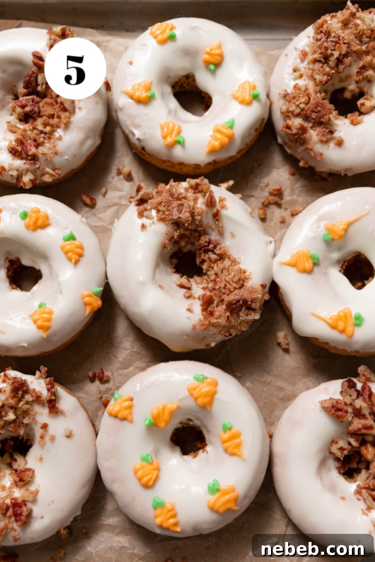 A baked carrot cake donut being dipped into a bowl of creamy cream cheese icing, part of the decorating process.