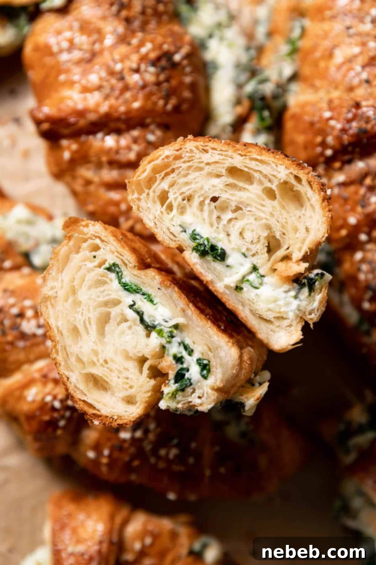 A delicious spinach croissant cut in half, revealing its creamy, melted cheese and vibrant spinach filling, topped with everything bagel seasoning.