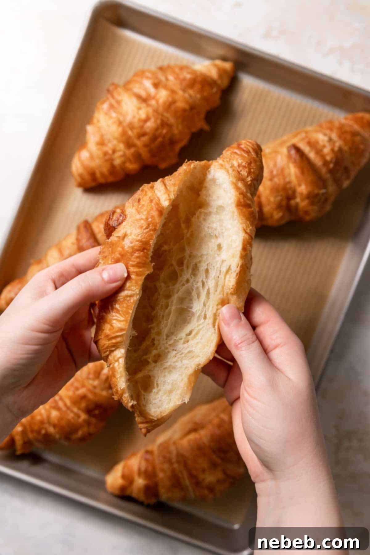 Hands carefully holding a croissant that has been sliced almost entirely open, creating a pocket for the filling.