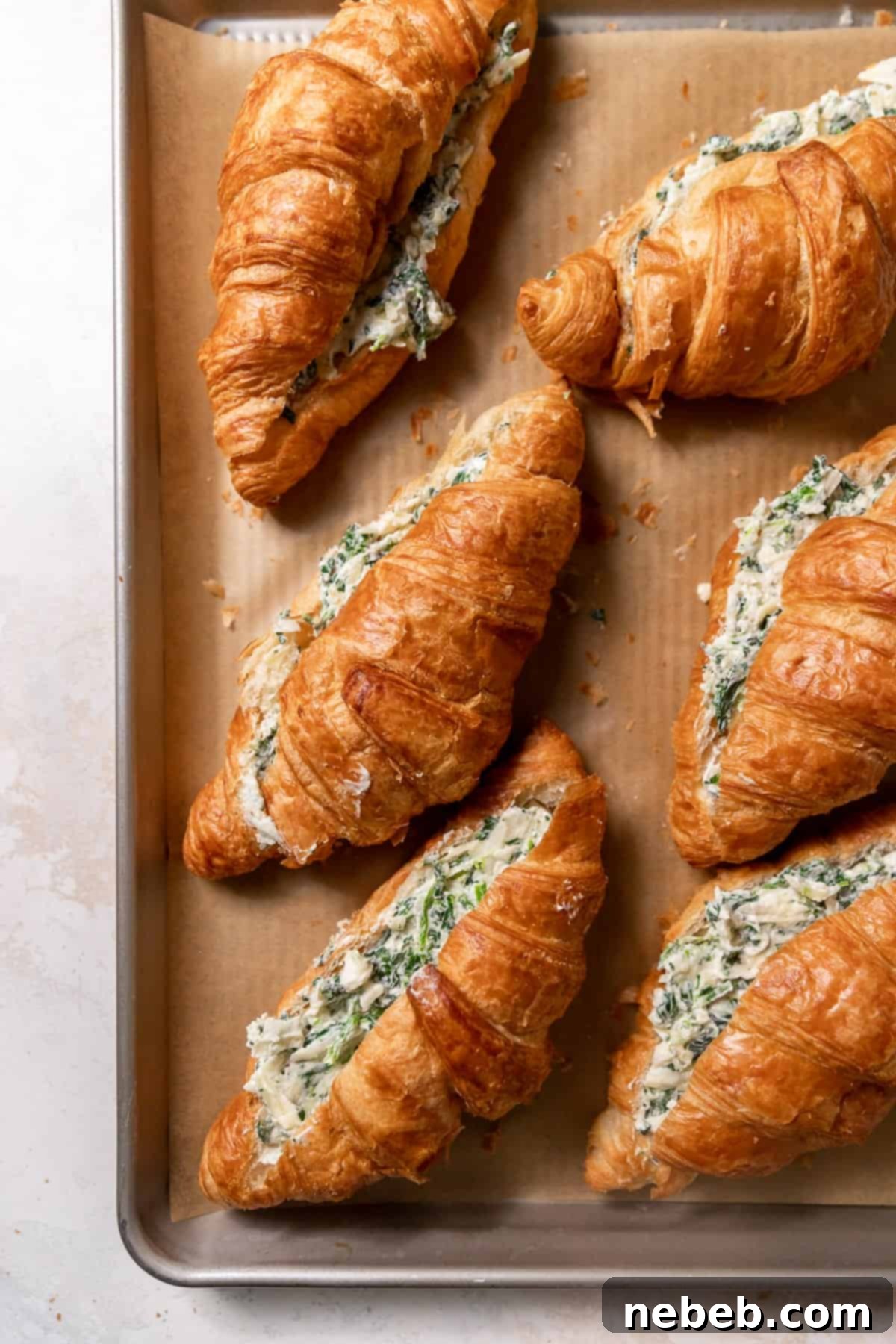 Croissants on a baking sheet, generously filled with the creamy spinach and cheese mixture, before baking.