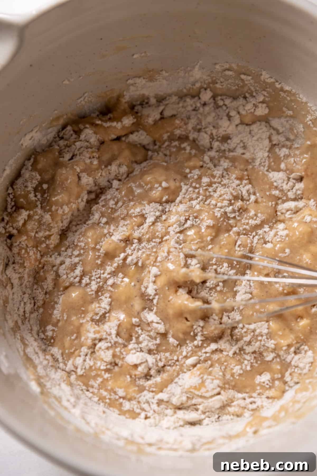 Banana donut batter being gently whisked in a mixing bowl to prevent overmixing.