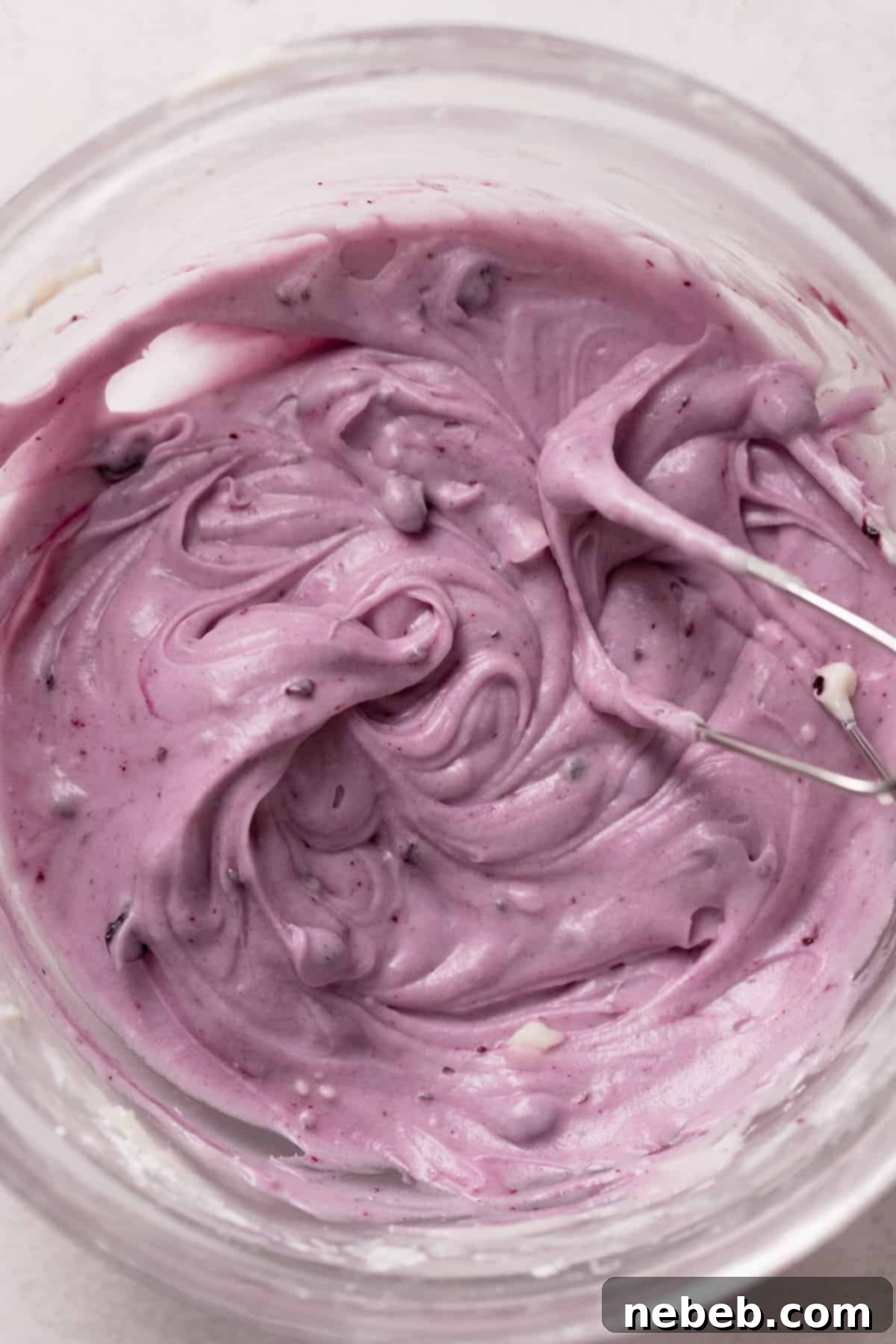 Smooth blueberry cream cheese frosting in a mixing bowl, ready to top the baked cinnamon rolls.