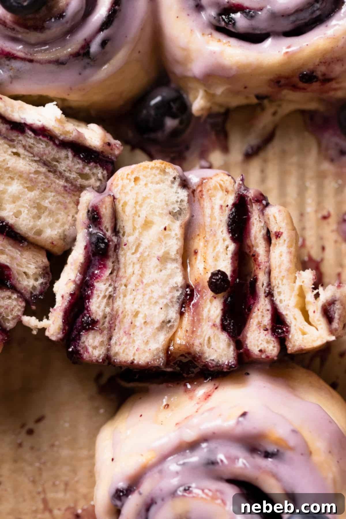A delicious blueberry sweet roll, cut in half to showcase the gooey blueberry jam filling and soft dough, with cream cheese frosting on top.