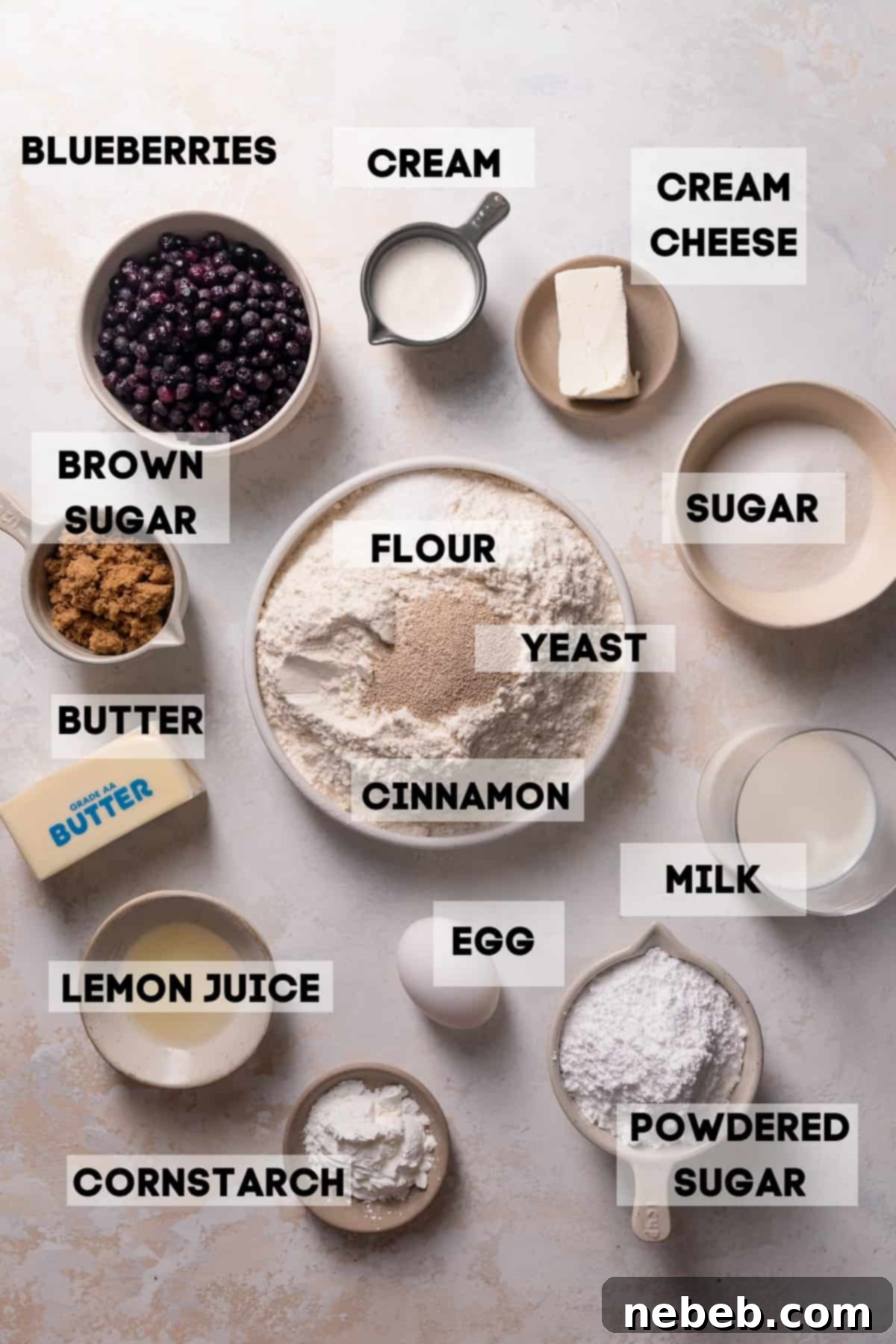 Bowls of fresh ingredients for making blueberry cinnamon rolls, including wild blueberries, flour, sugar, and yeast.