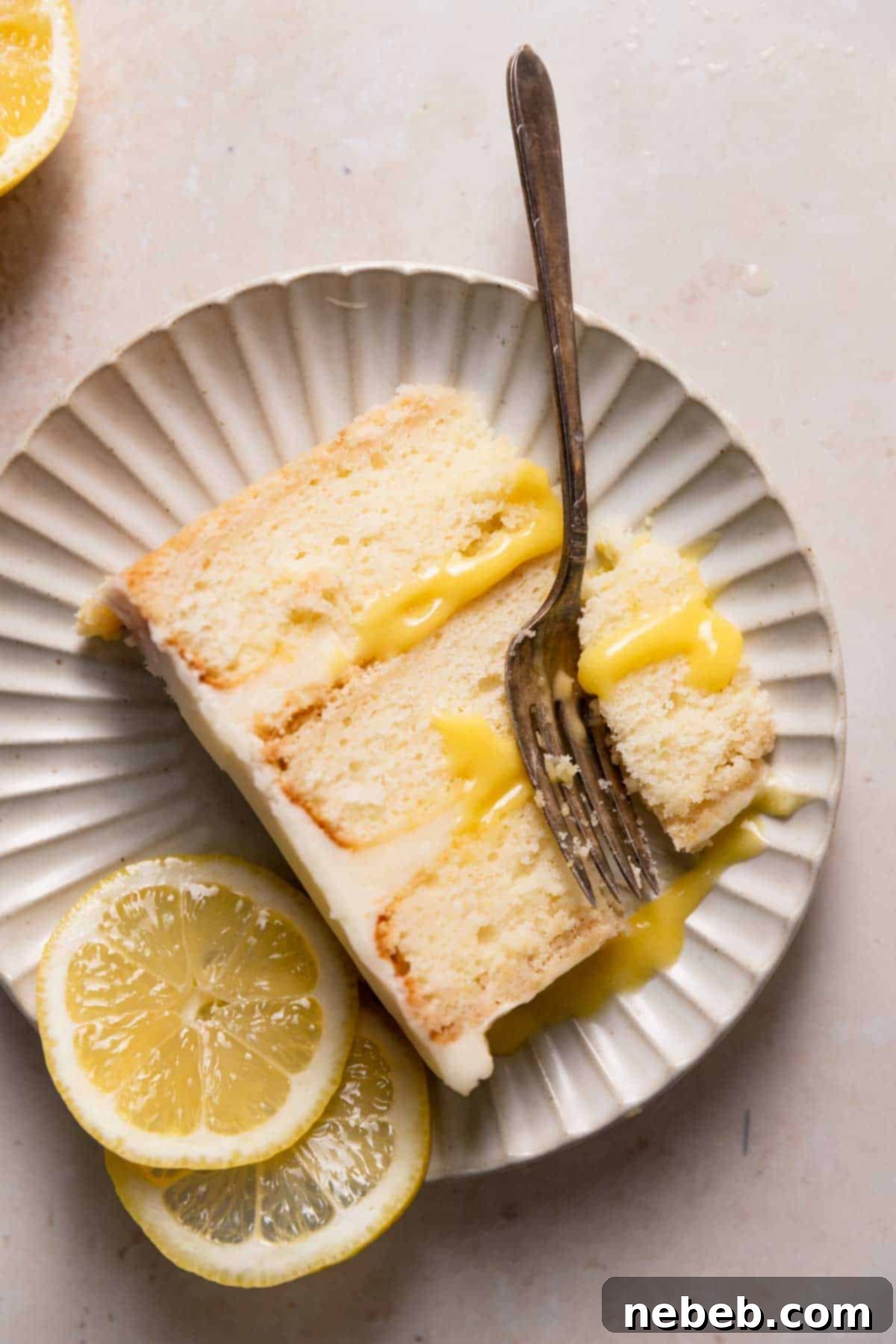 A delectable slice of lemon bar cake on a white plate, garnished with fresh lemon slices, highlighting its layers and inviting texture.