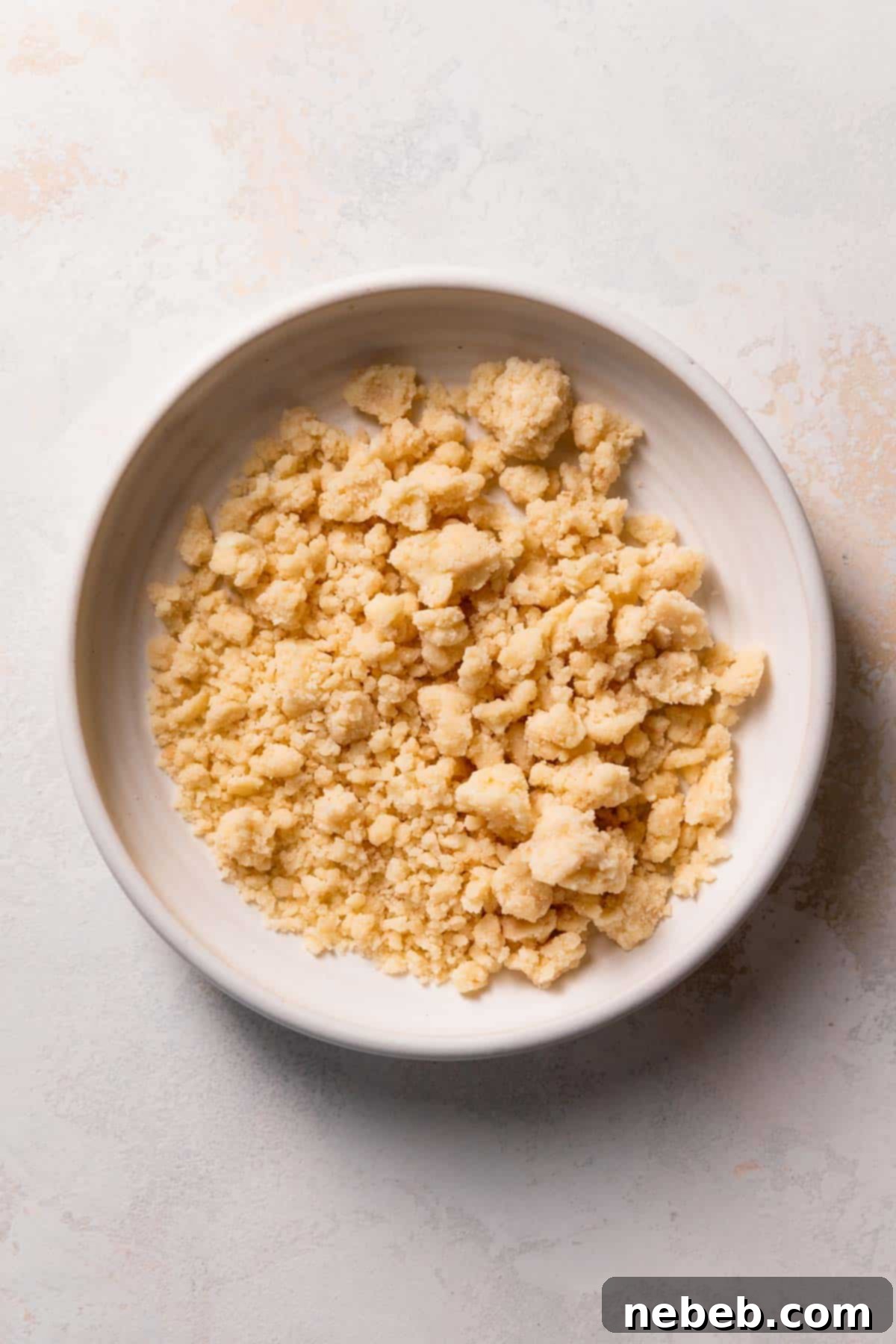 A bowl filled with crumbly shortbread mixture, ready to be pressed into the cake pans for the crust.