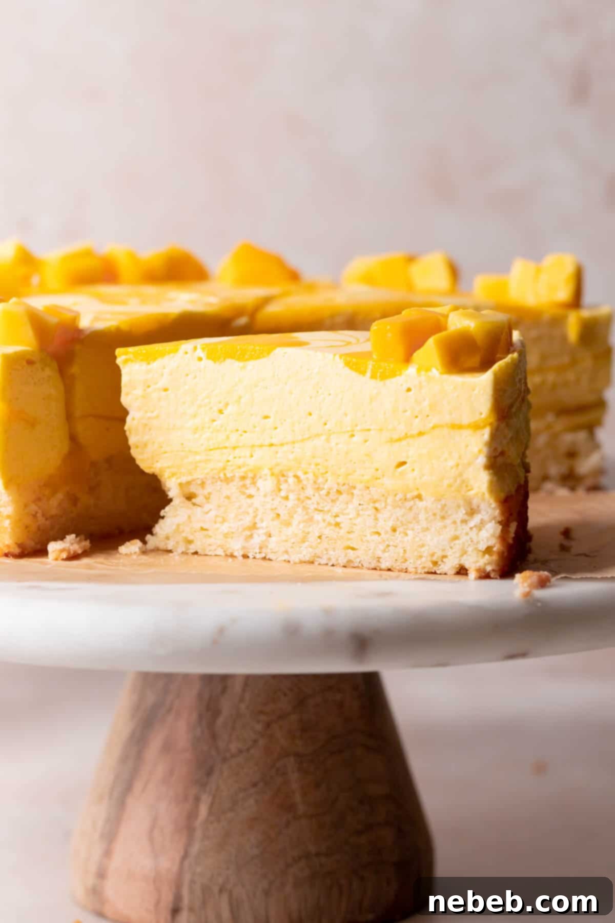 A slice of mango mousse cake topped with fresh mango on a white cake stand, highlighting its layers.