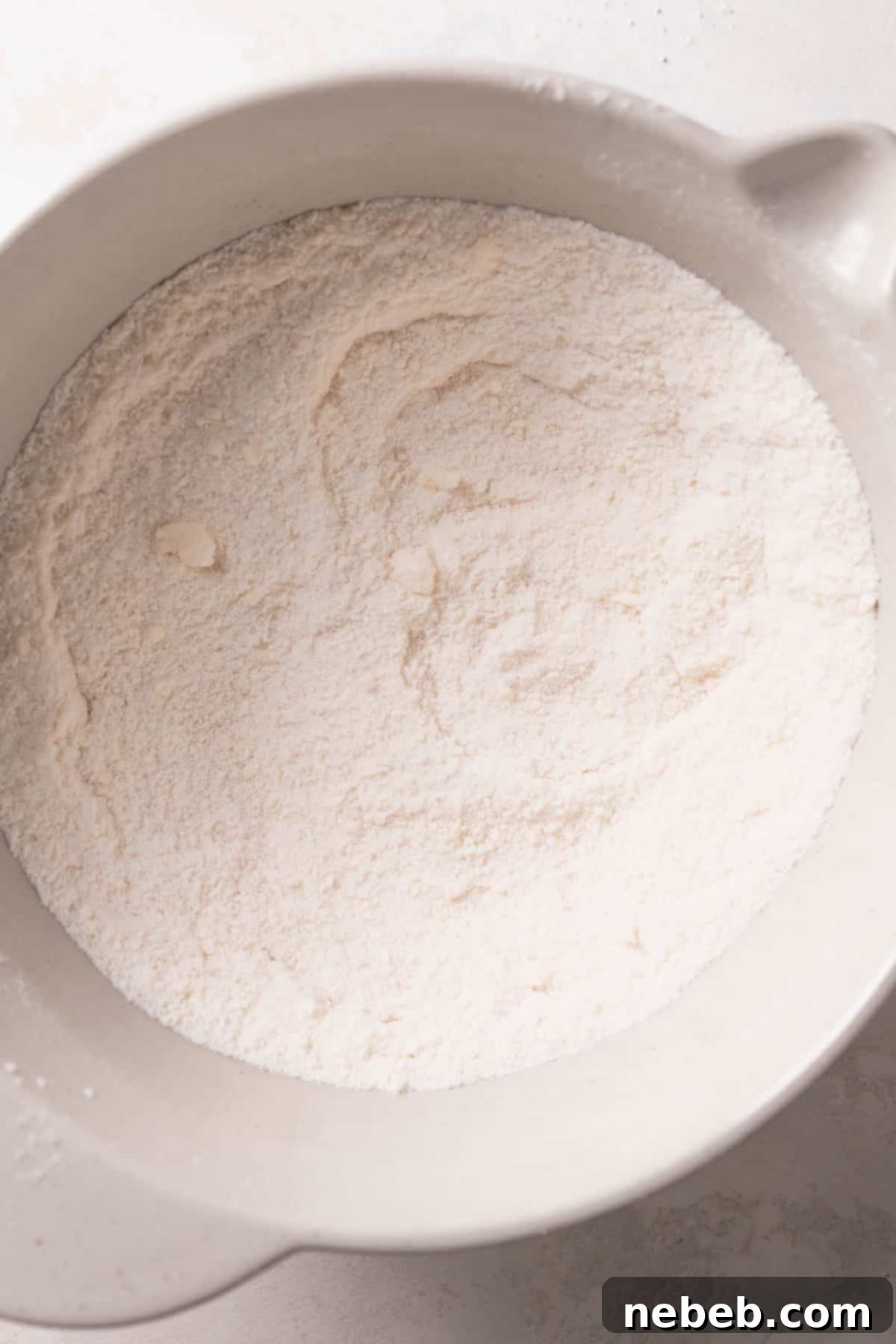 Butter and dry ingredients are mixed together in a bowl, resembling coarse sand.