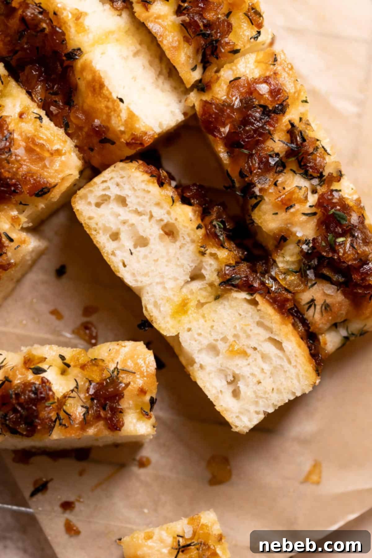 Slices of fluffy caramelized onion focaccia on parchment paper, showcasing golden crust and onion topping.