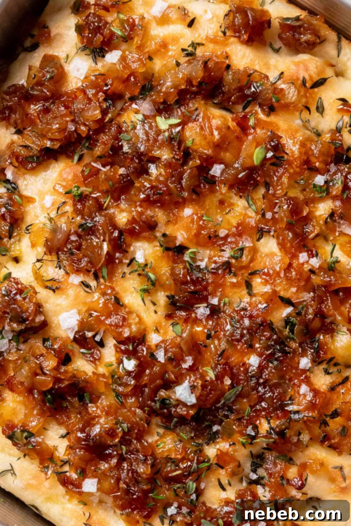 Freshly baked focaccia with caramelized onions, fresh thyme, and flaky sea salt on top, resting on a cooling rack.