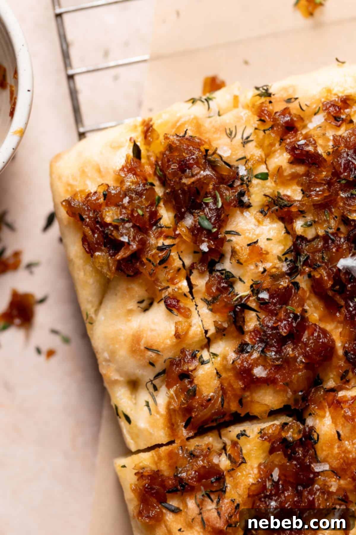 A large piece of french onion focaccia bread, topped with golden caramelized onions and fresh thyme, resting on a wire cooling rack.