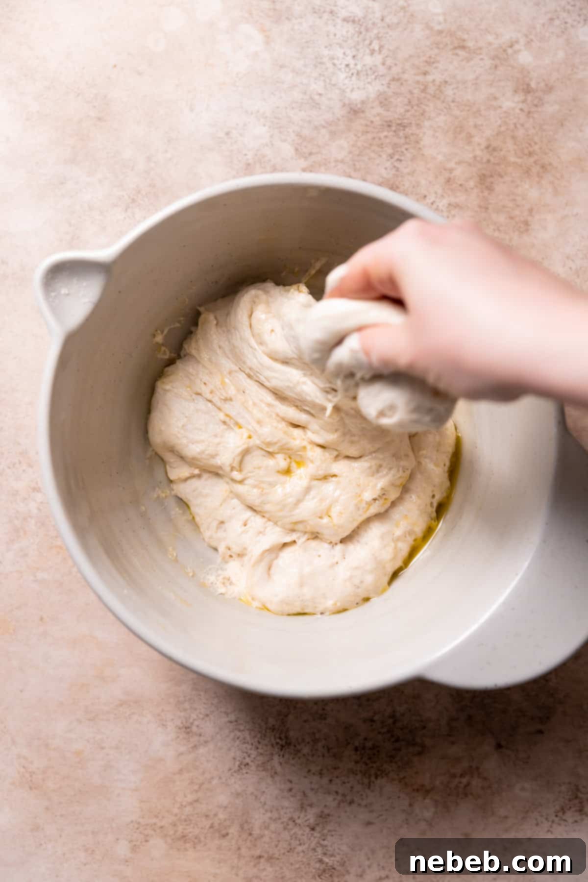 A hand gently stretching and folding the sticky focaccia dough in a bowl, a key step for developing gluten.