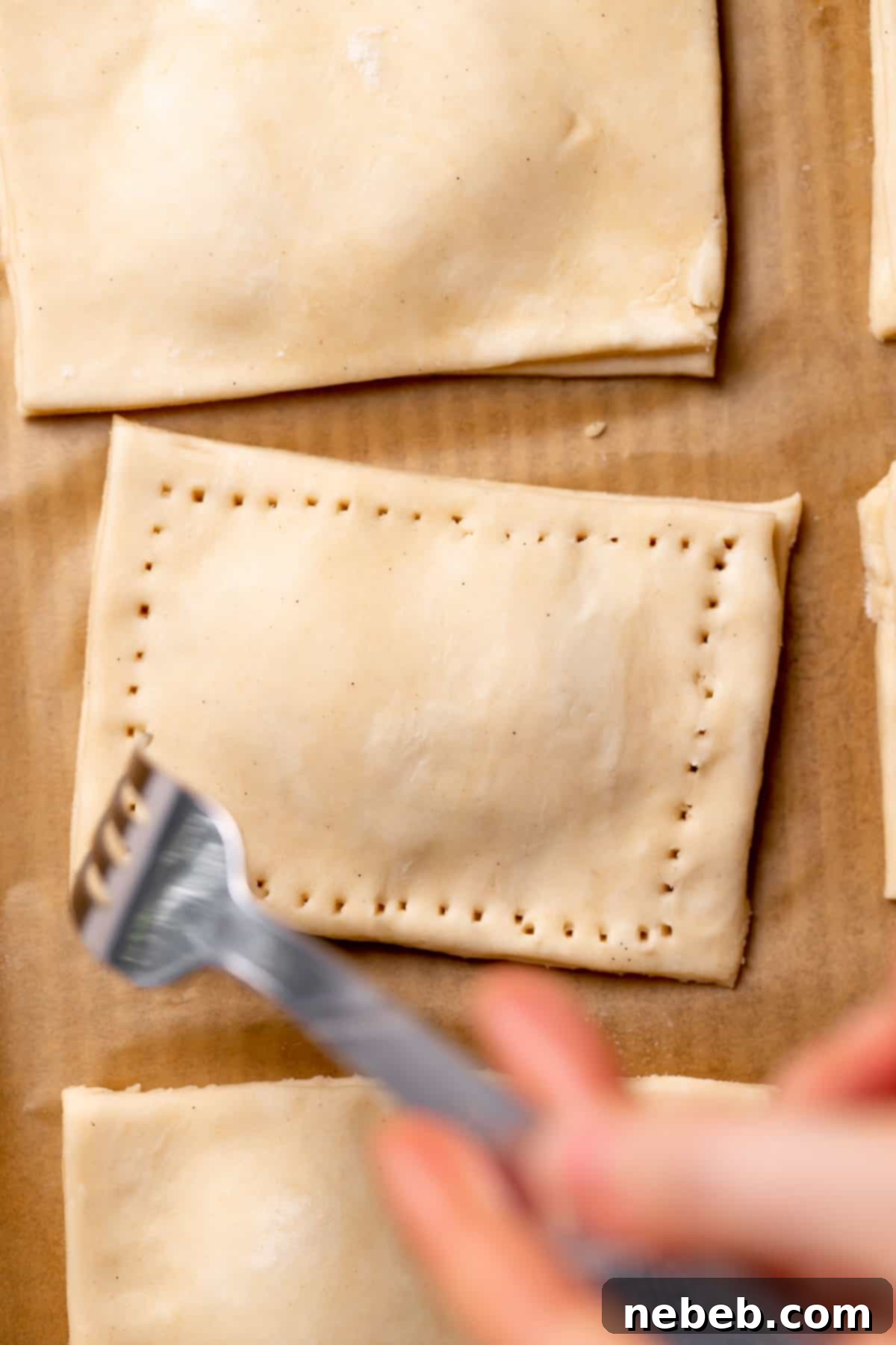 A fork crimping the edges of the pop tarts to seal them, showing steam vents.