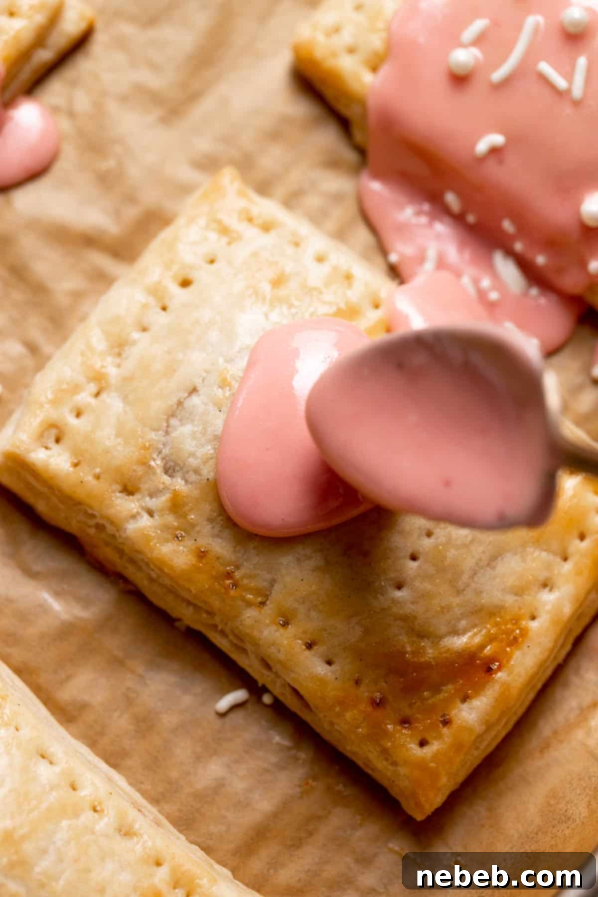 Spoon-glazing a baked pop tart with a smooth, pink vanilla glaze, ready for sprinkles.