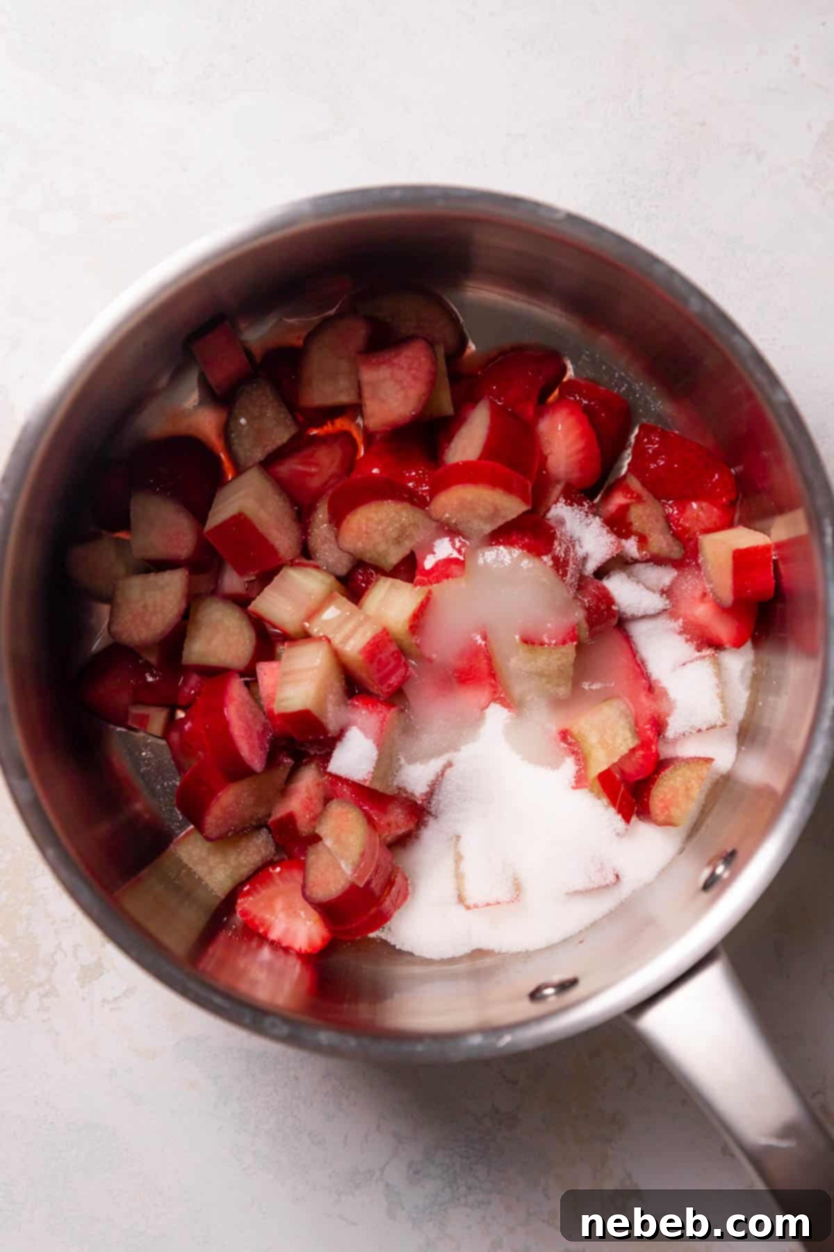 Strawberries and rhubarb simmering in a pot with sugar, creating homemade jam.
